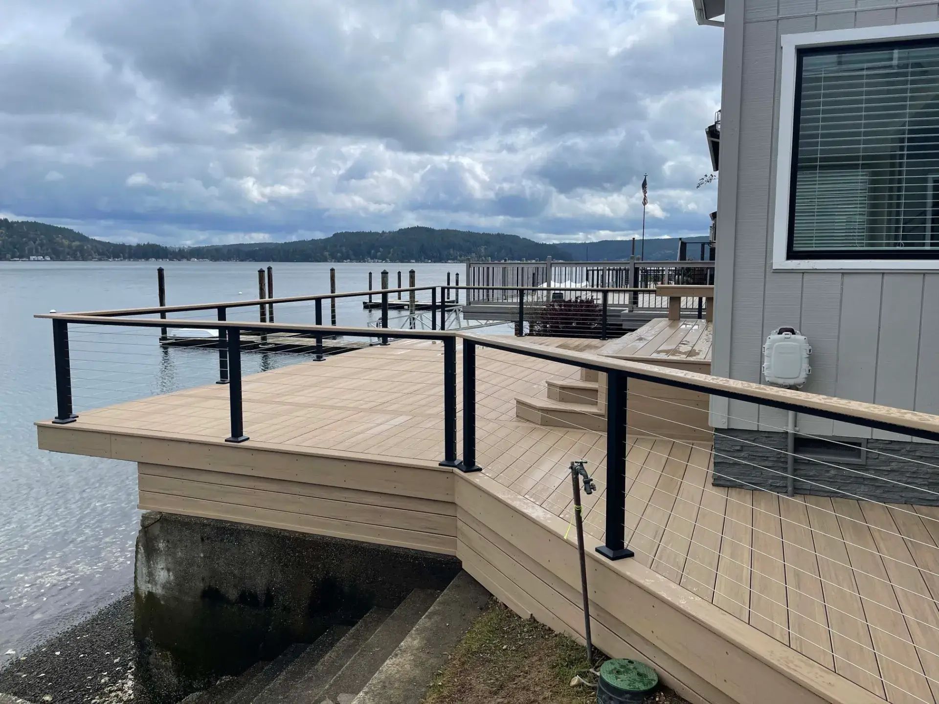 Wooden dock deck beside calm water under cloudy sky, with railings and a building wall on the right