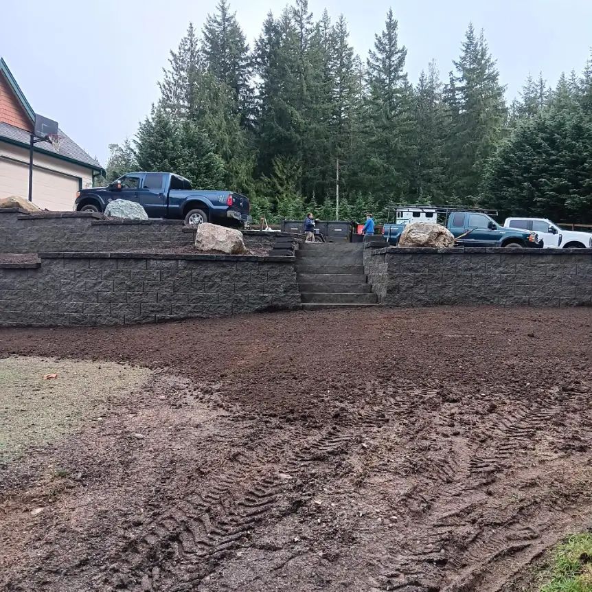Gravel terrace with stone steps, parked pickup trucks, and pine trees behind a muddy foreground
