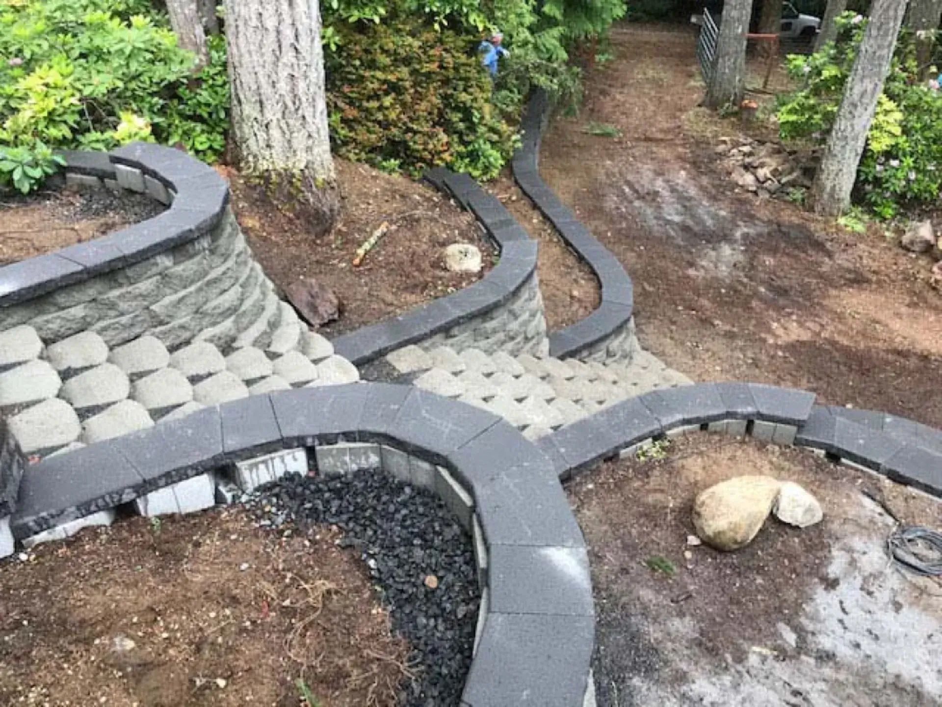 Curved stone garden retaining walls and paths around trees and wet soil in a landscaped yard