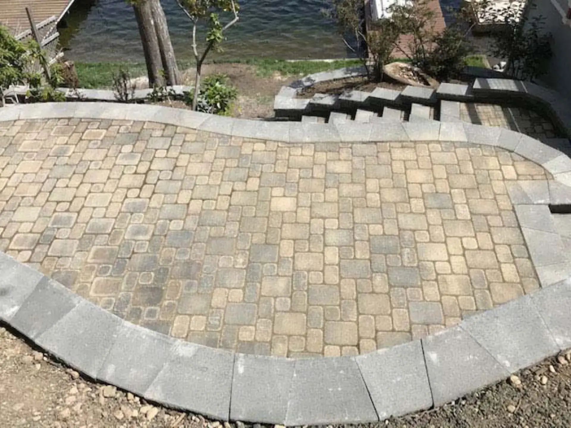 Curved stone-paver patio with concrete border beside steps and landscaped garden
