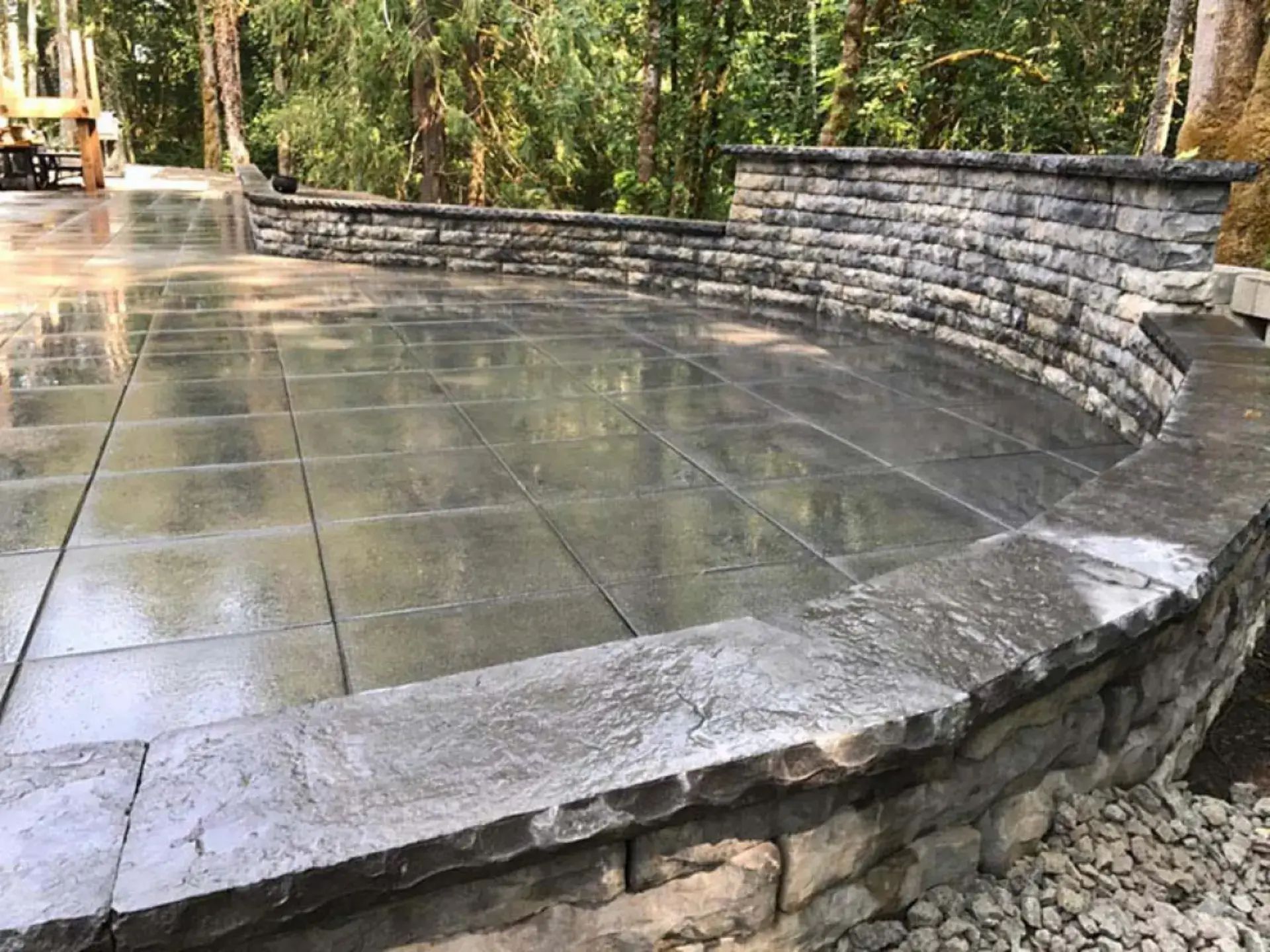 Curved stone amphitheater seating around a wet tiled plaza in a wooded park
