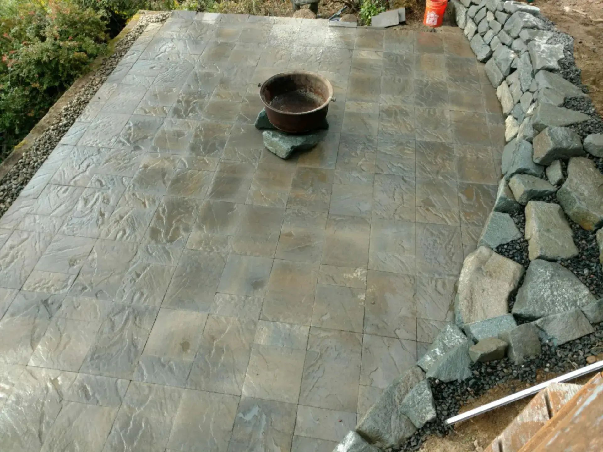 Stone patio under construction with a wheelbarrow in the center and stacked rocks along one side