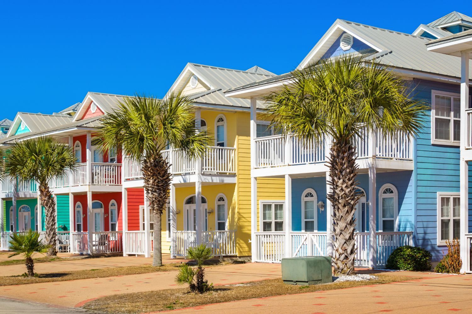 Row of colorful beach houses with palm trees and a bright blue sky.
