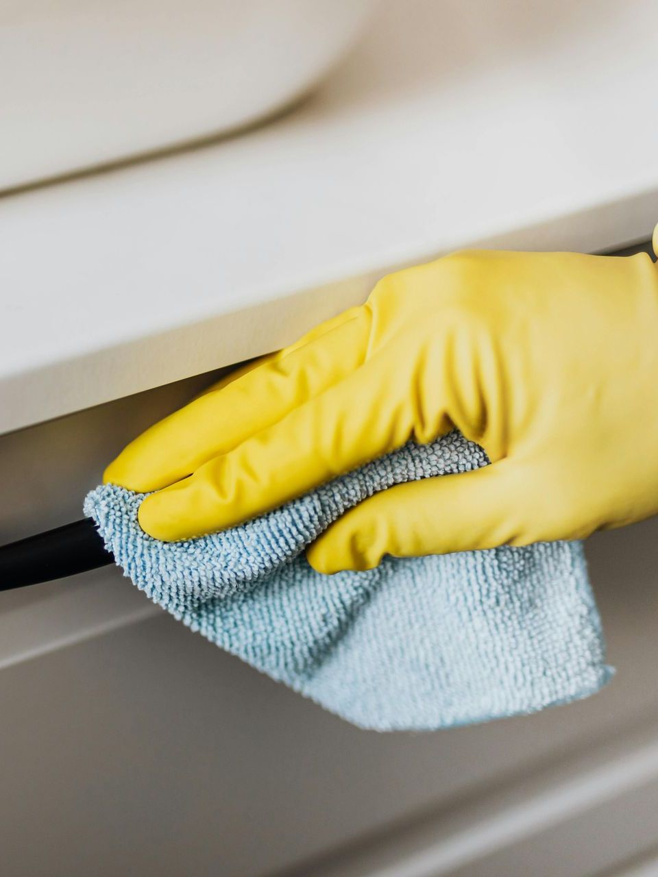Hand in yellow glove wiping cabinet with blue cloth.