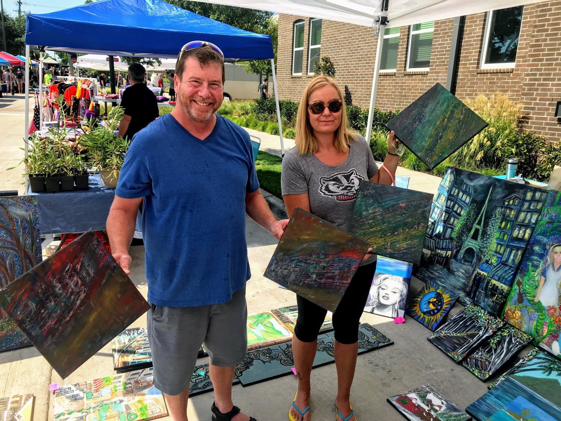 A man and a woman are standing next to each other holding paintings.