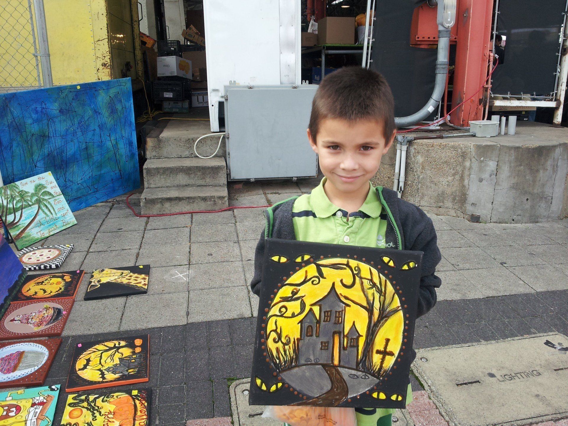 A young boy is holding a painting of a haunted house