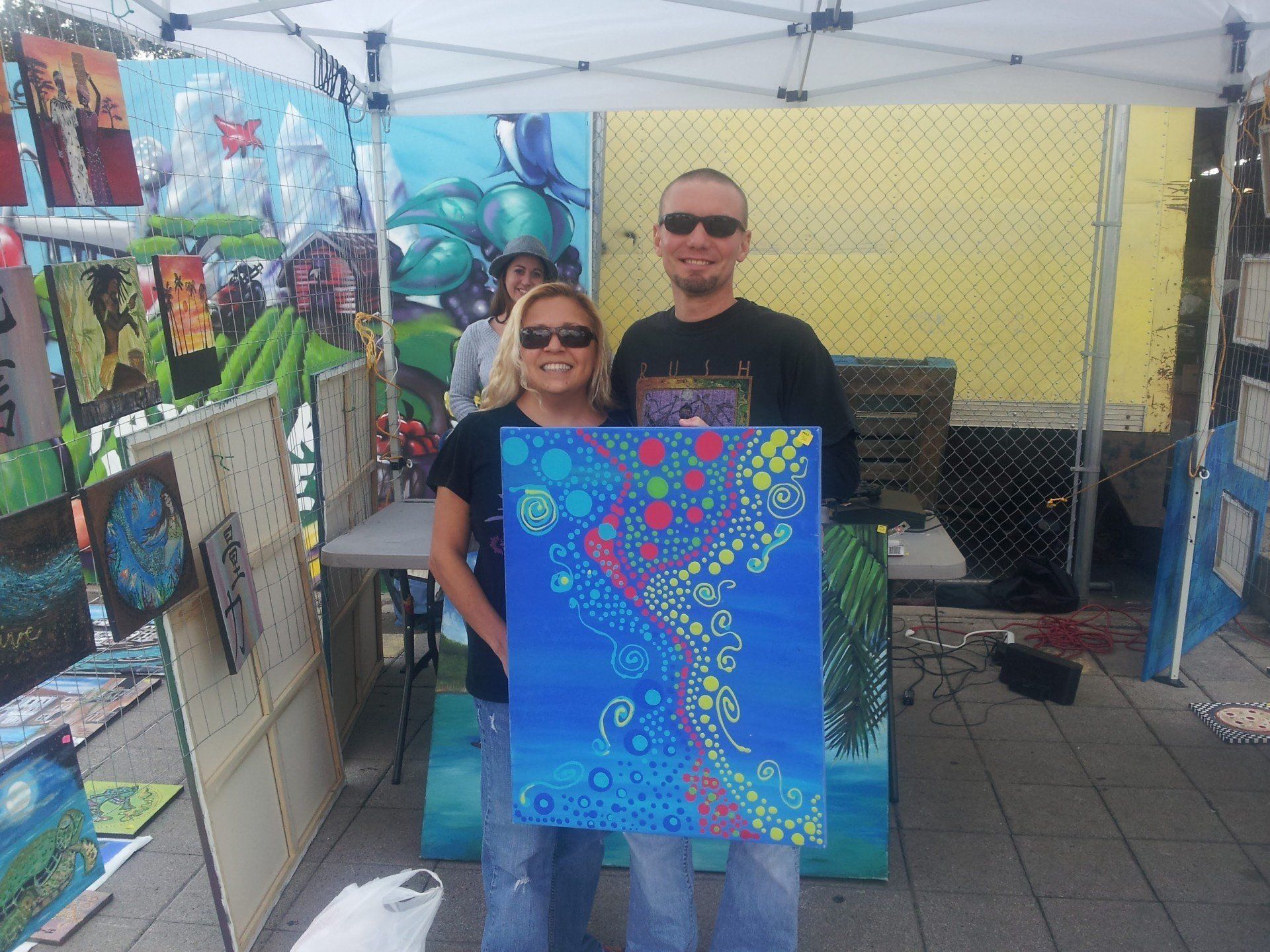 A man and a woman holding a painting in front of a tent