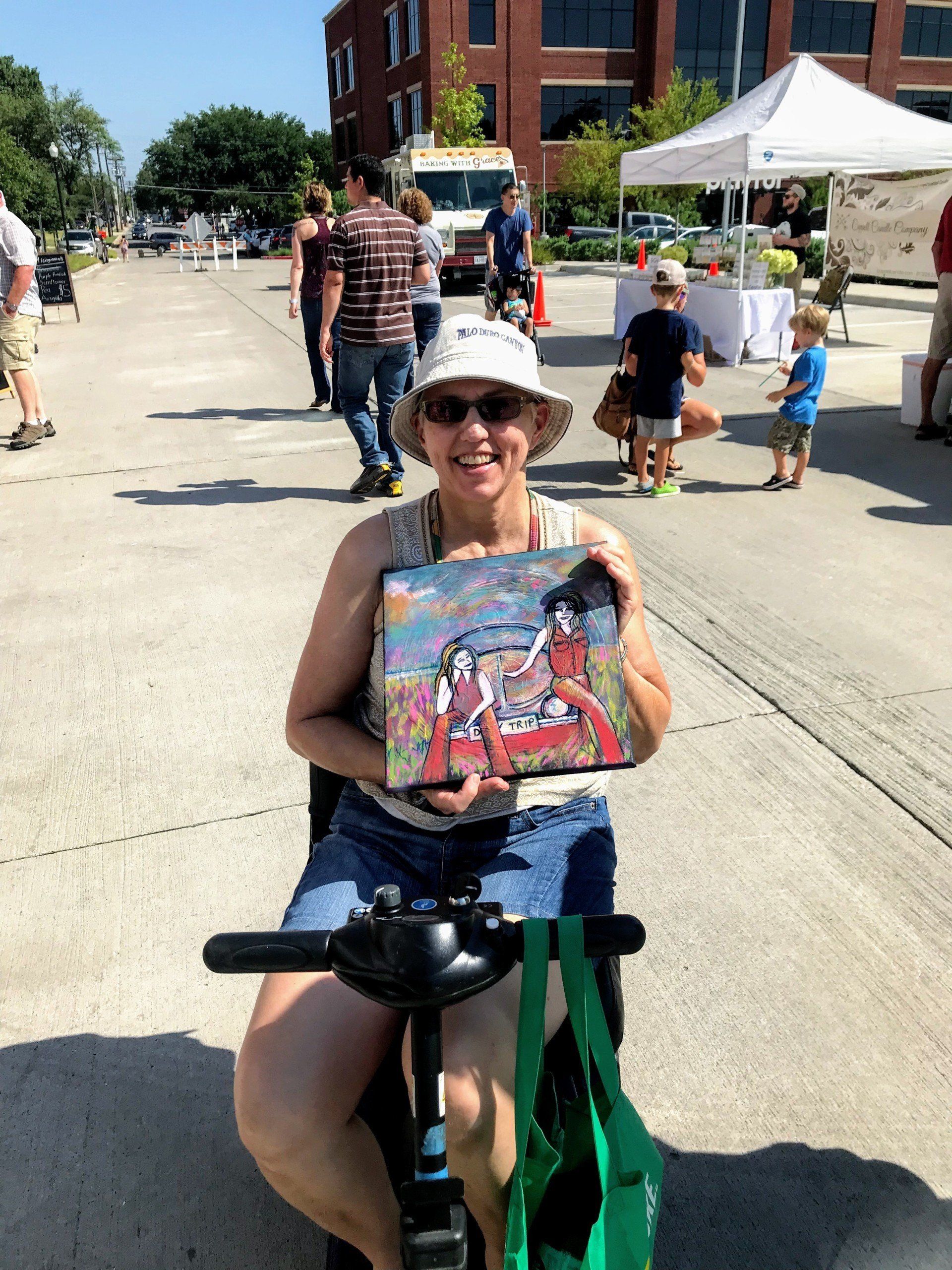 A woman is sitting on a scooter holding a painting.