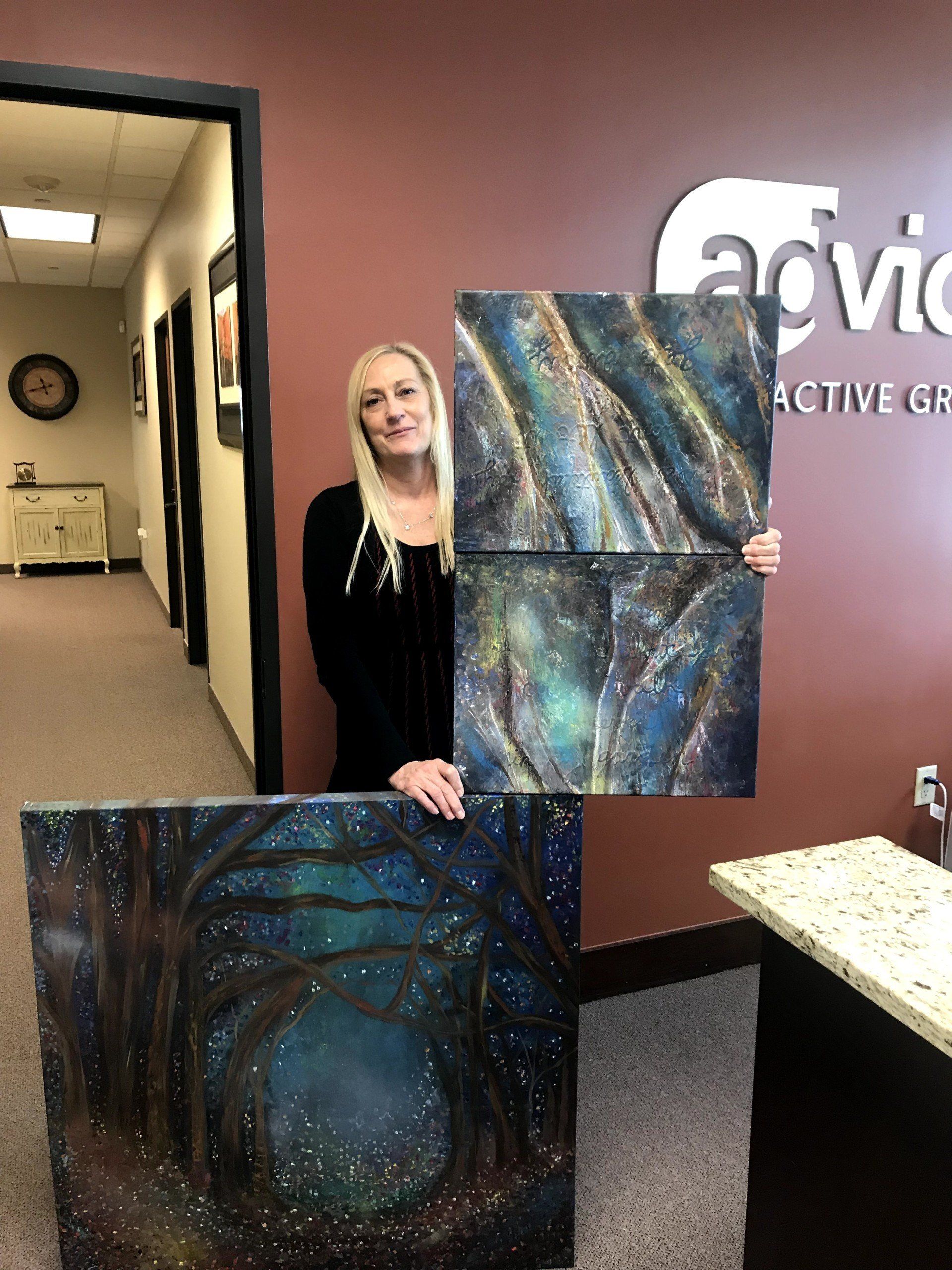 A woman is holding two paintings in front of a sign that says advice