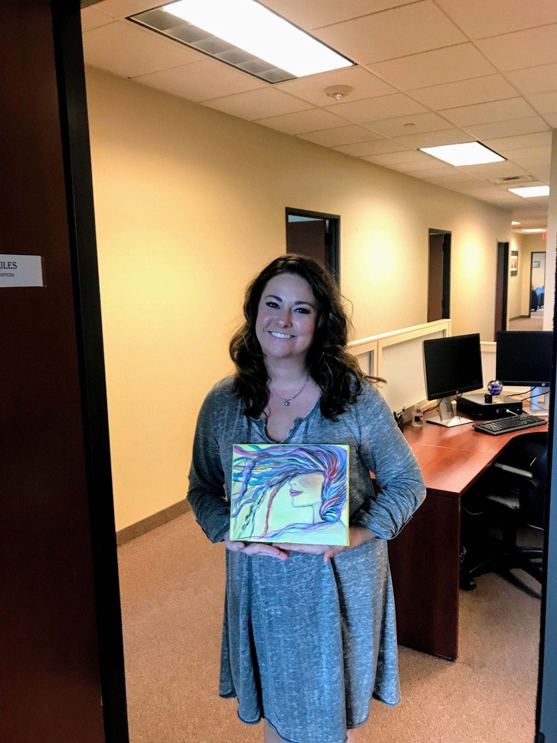 A woman is holding a painting in an office.