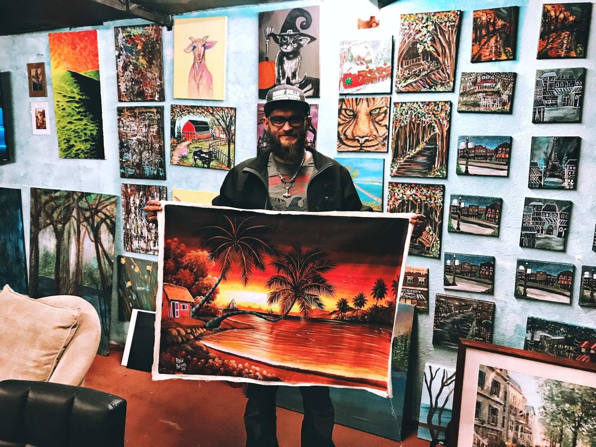 A man is holding a large painting in front of a wall of paintings