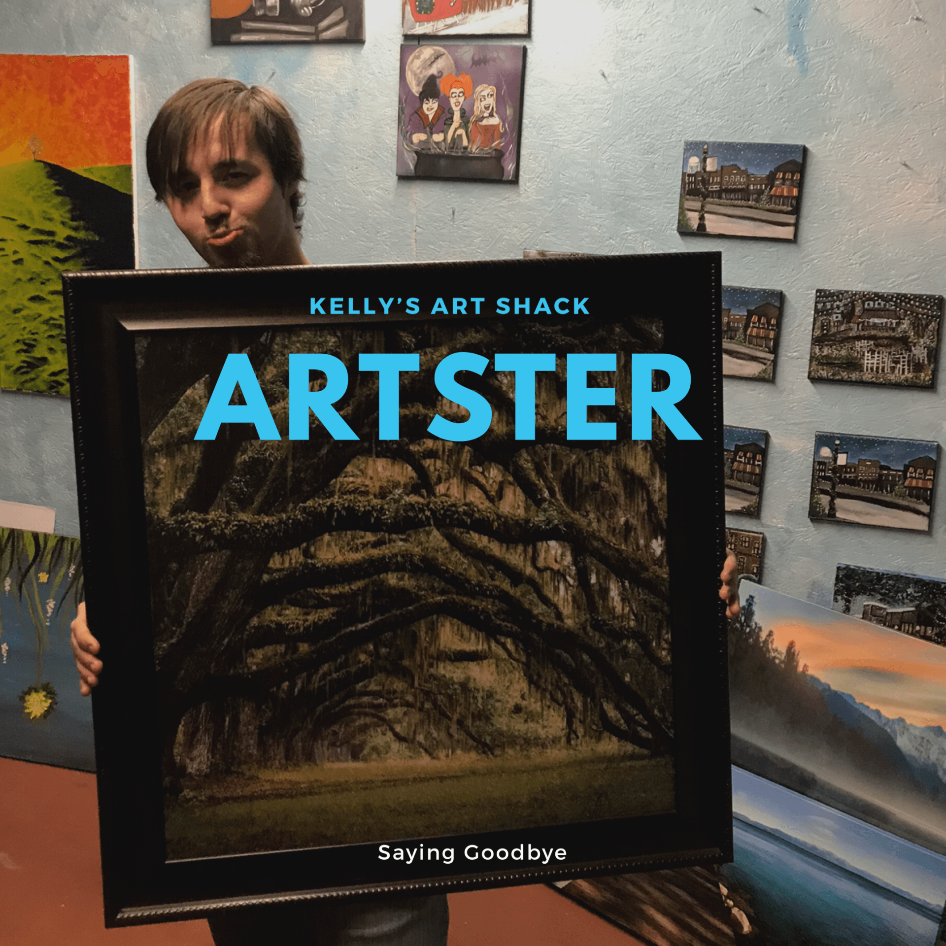 A man is holding a framed picture that says kelly 's art shack