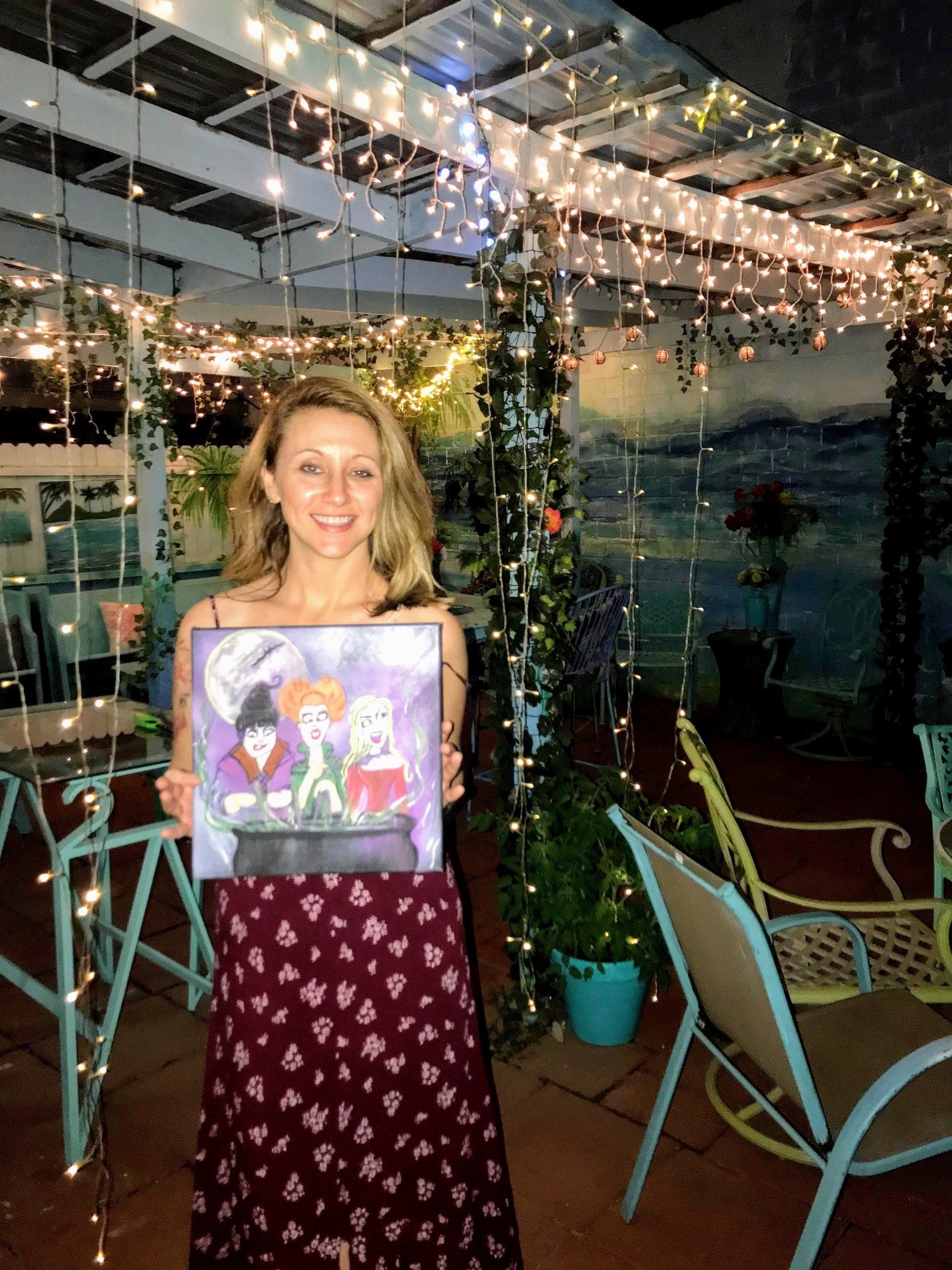 A woman is holding a painting of three girls on a patio