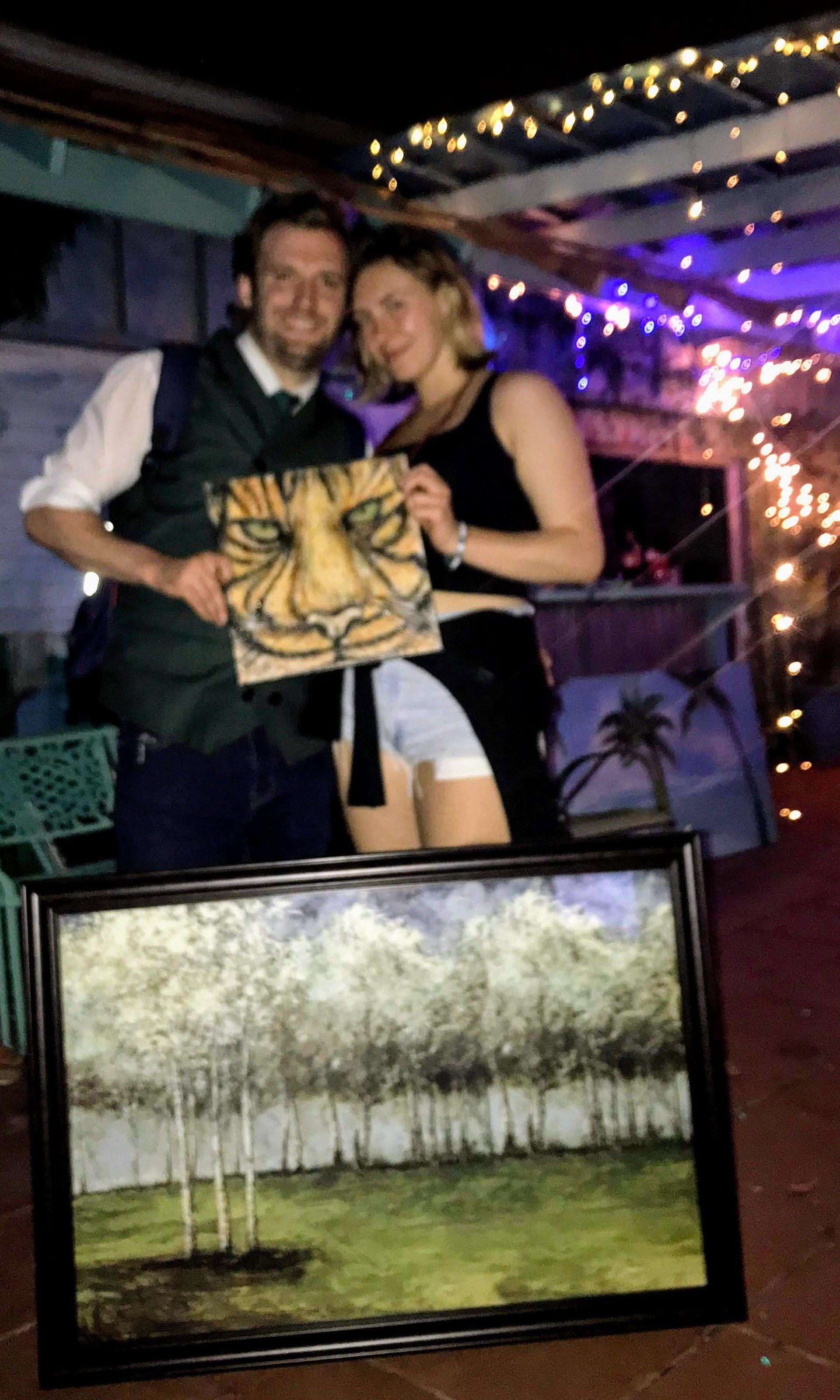 A man and a woman are holding a framed painting