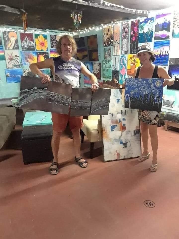 Two women are standing in a room holding paintings.
