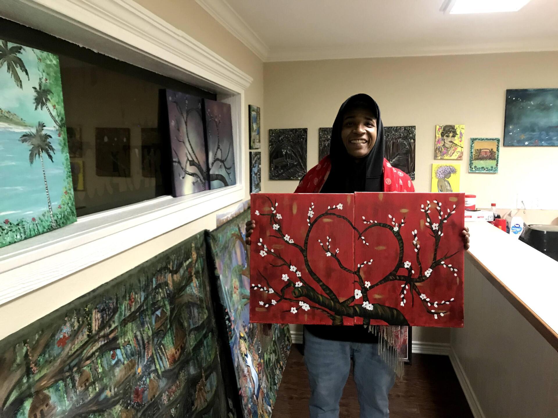 A man is holding a painting of a heart on a tree branch