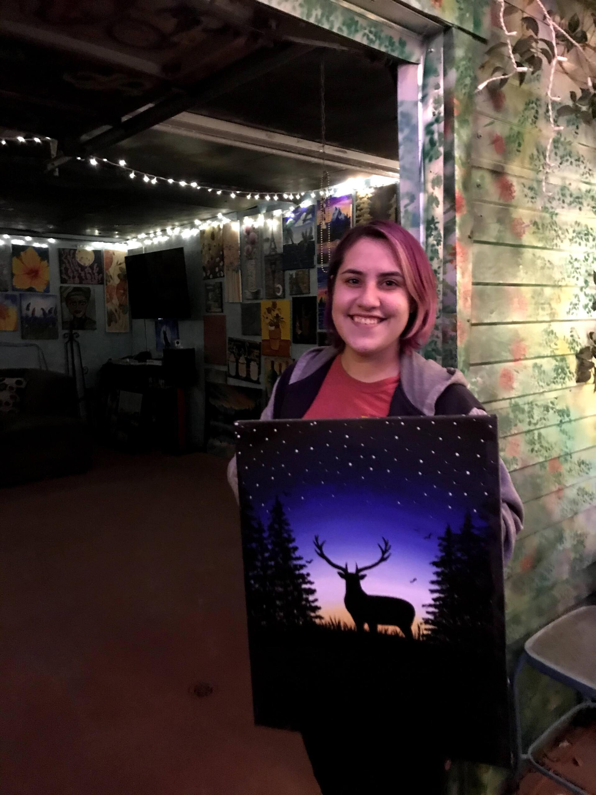 A woman is holding a painting of a deer in the woods