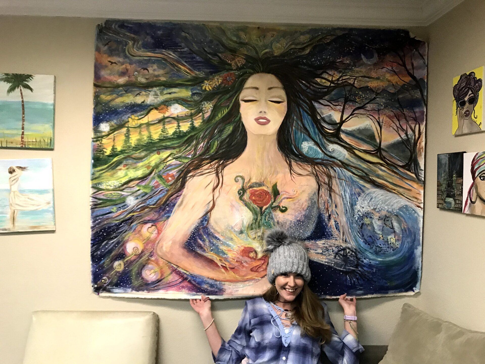 A woman is standing in front of a large painting of a woman.