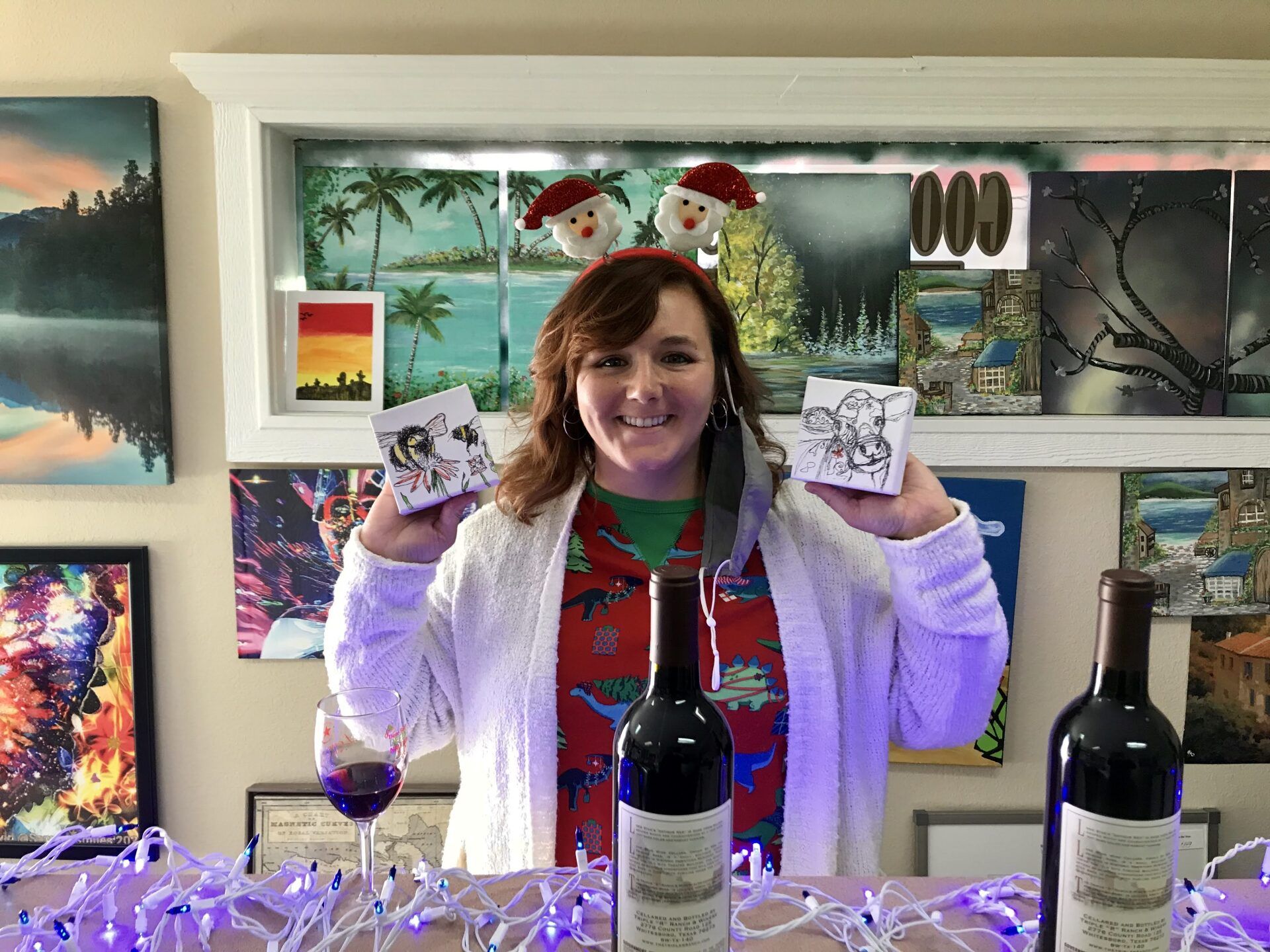 A woman is standing in front of a table with three bottles of wine and a glass of wine.