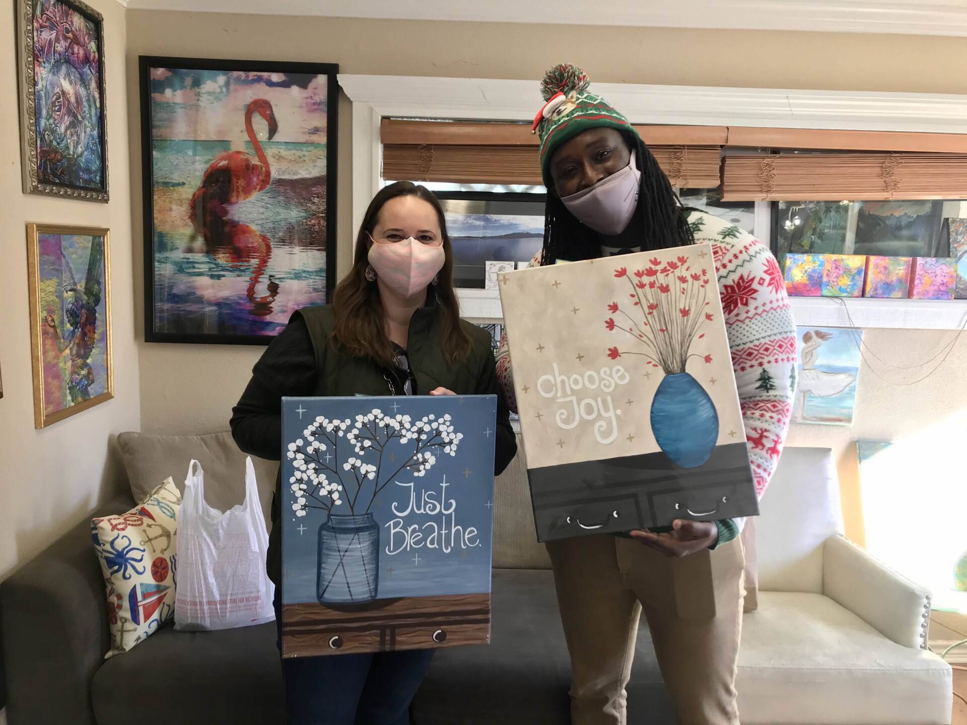 Two people wearing masks are holding paintings in a living room.