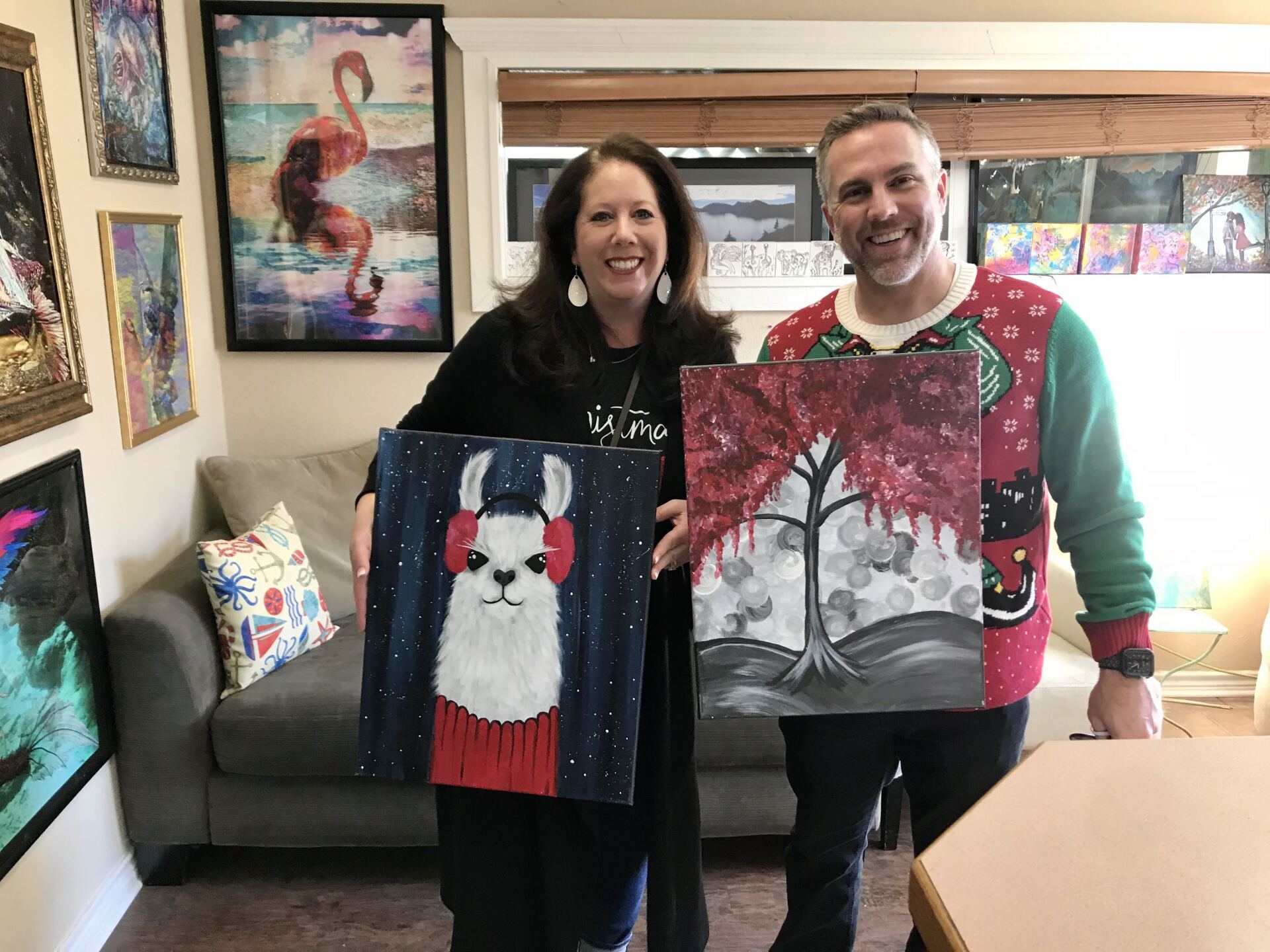 A man and a woman are holding two paintings in a living room.