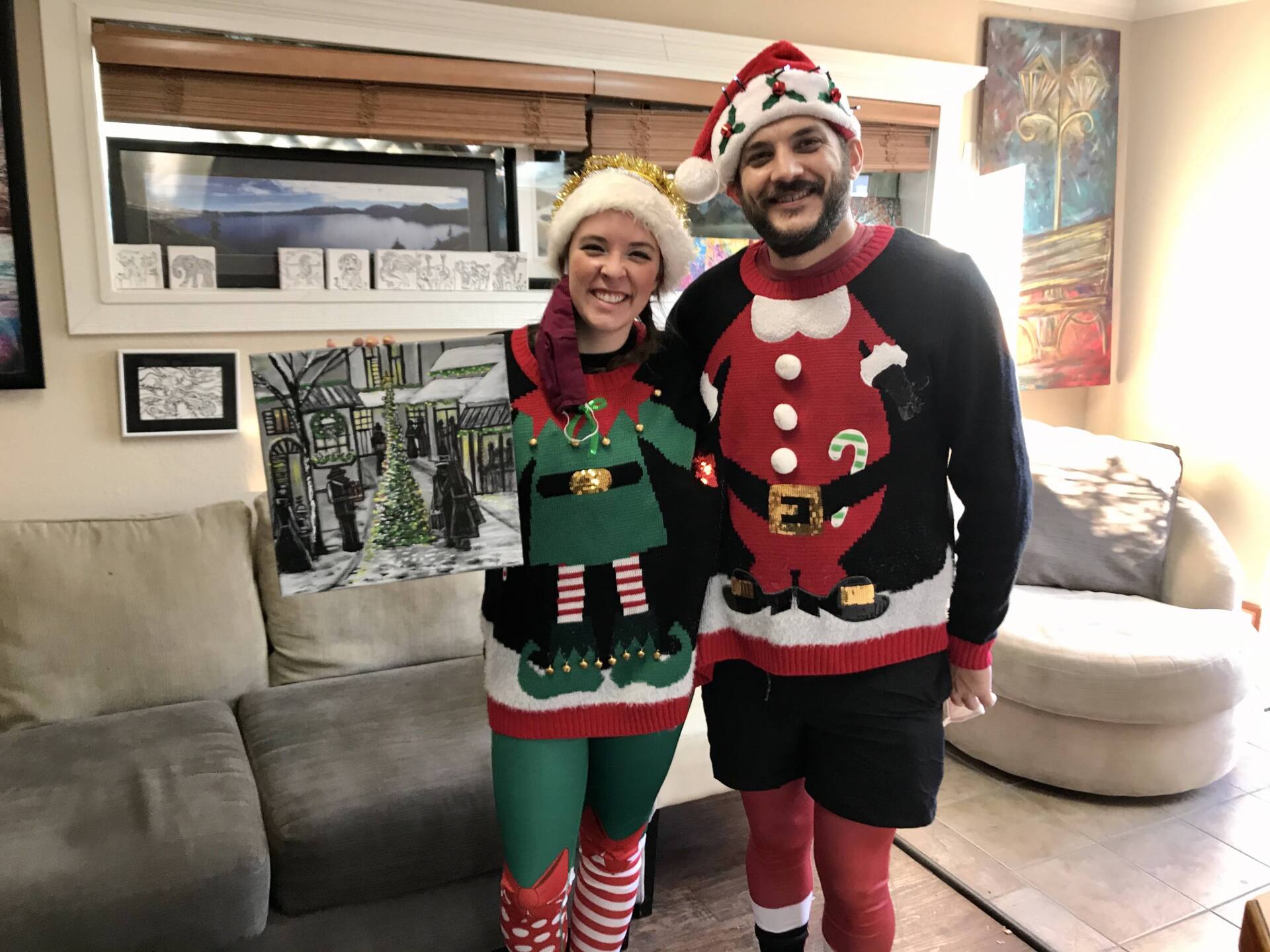 A man and a woman are standing next to each other in a living room wearing christmas sweaters.
