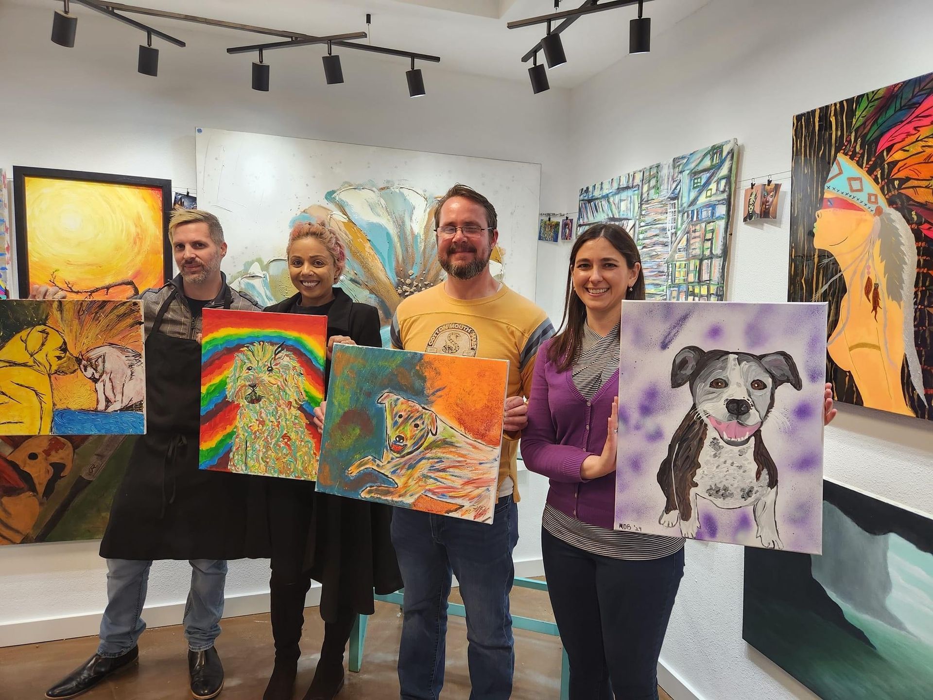 A group of people are standing in a room holding paintings of dogs.