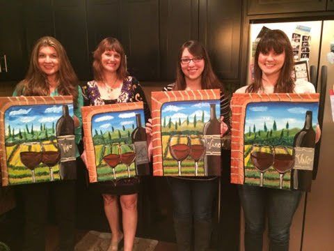 Four women are standing next to each other holding paintings of wine bottles and glasses.