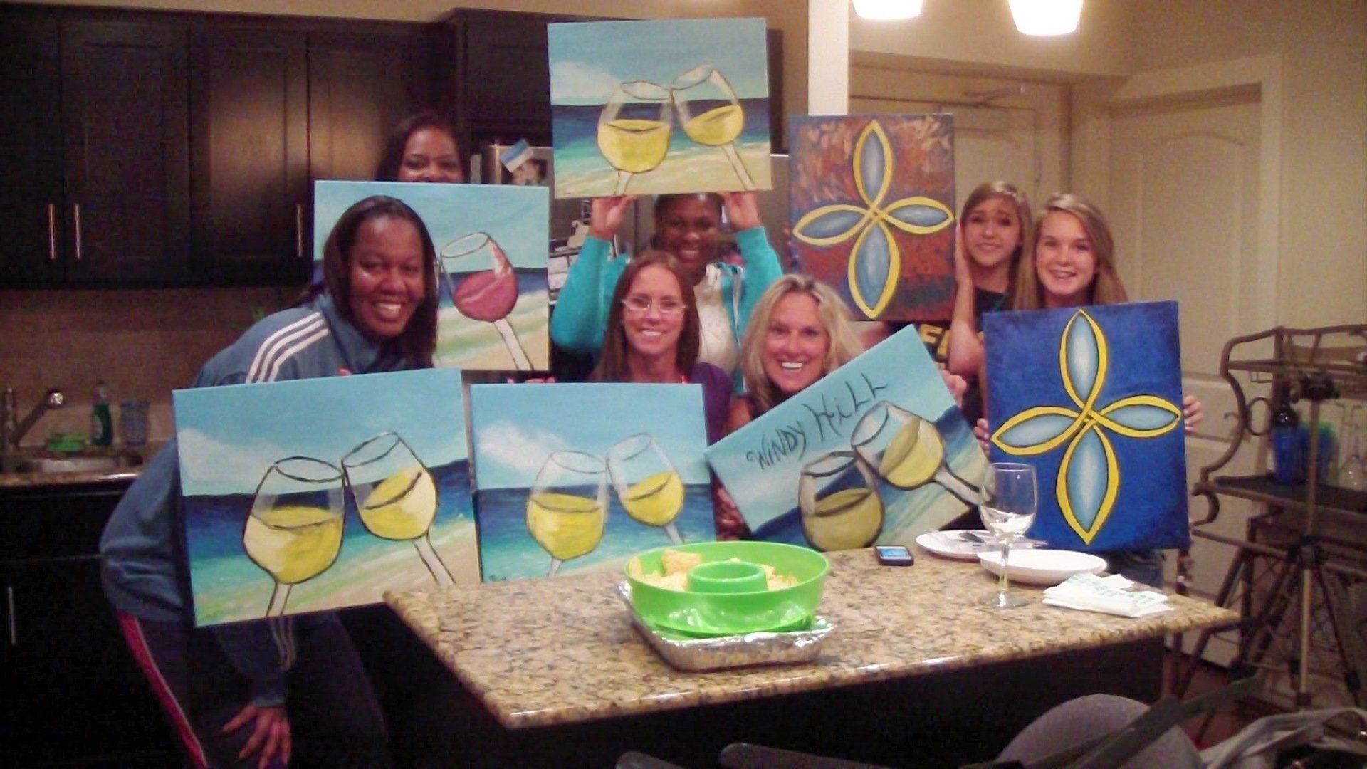 A group of women holding up paintings of wine glasses