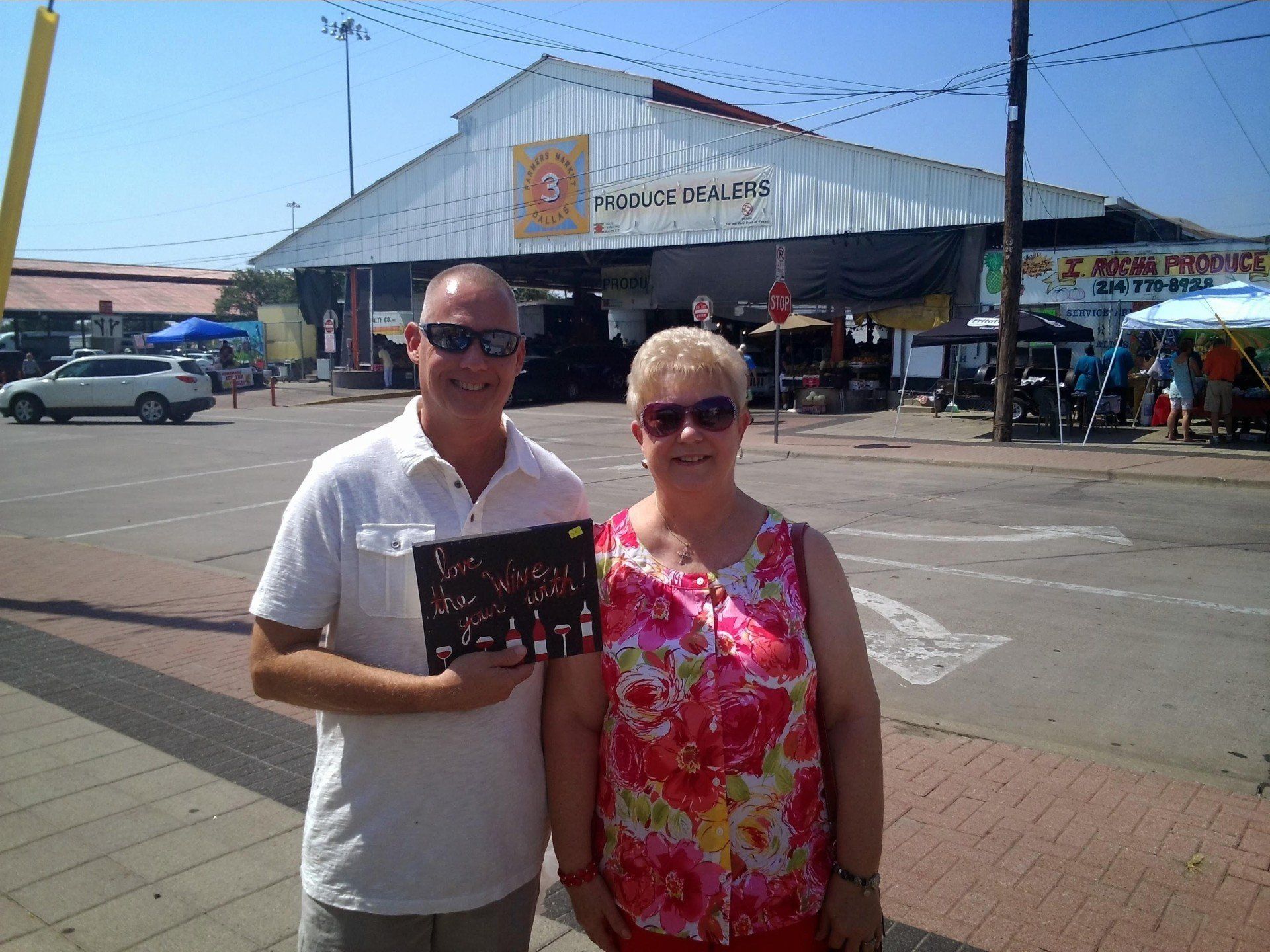 A man and a woman are posing for a picture in front of a building that says farm produce