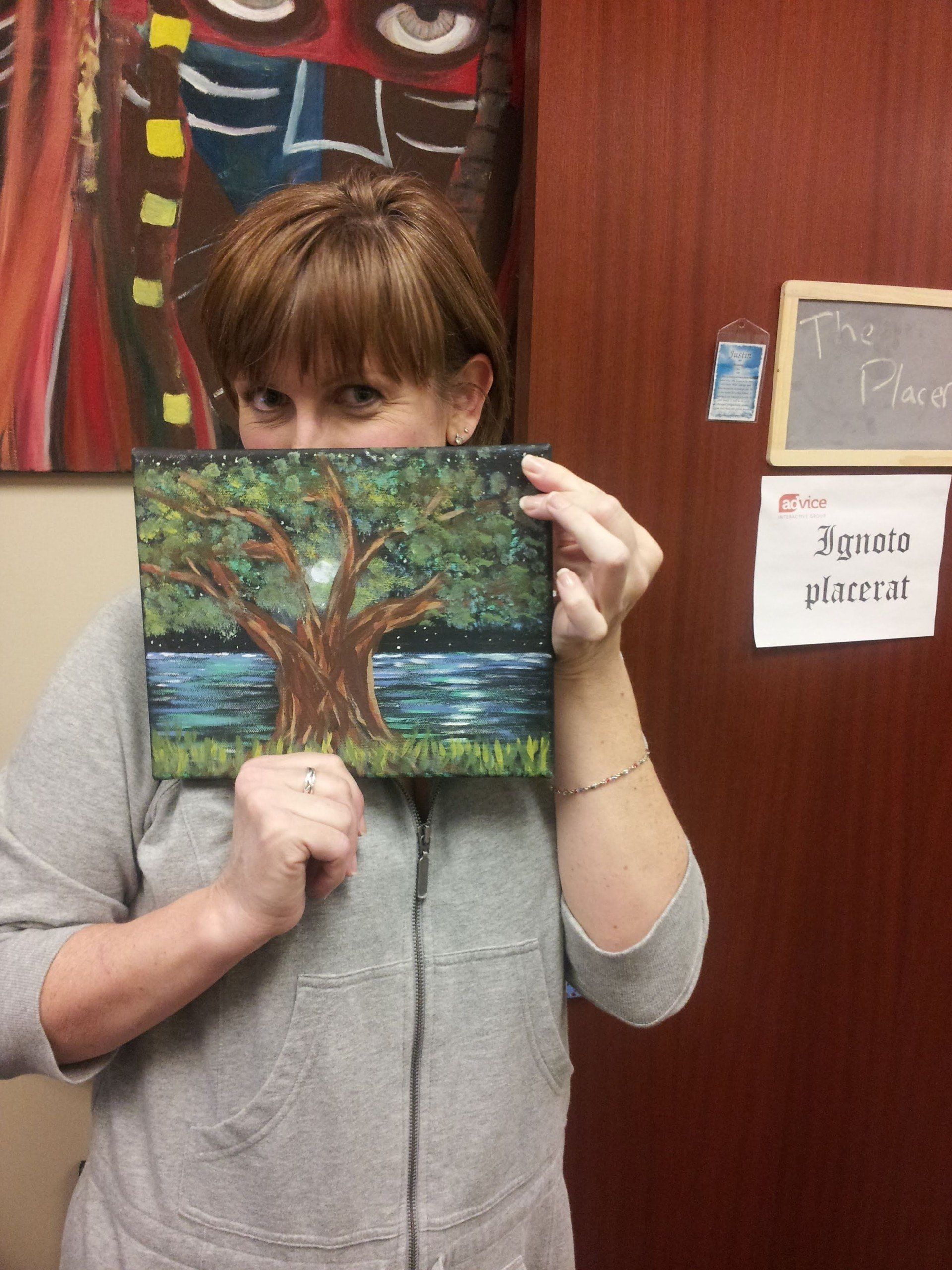A woman covering her face with a painting of a tree