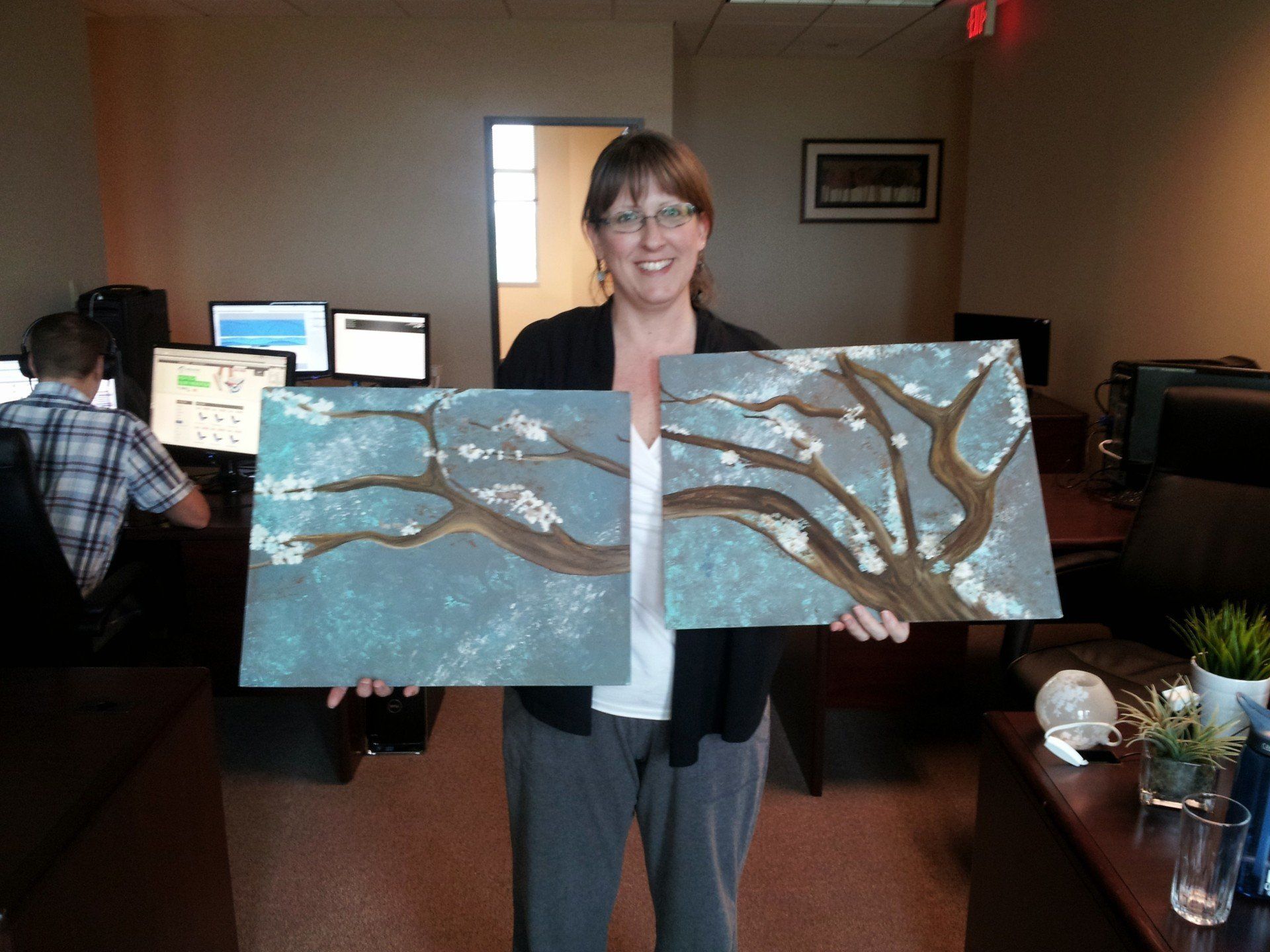 A woman is holding two paintings of a tree