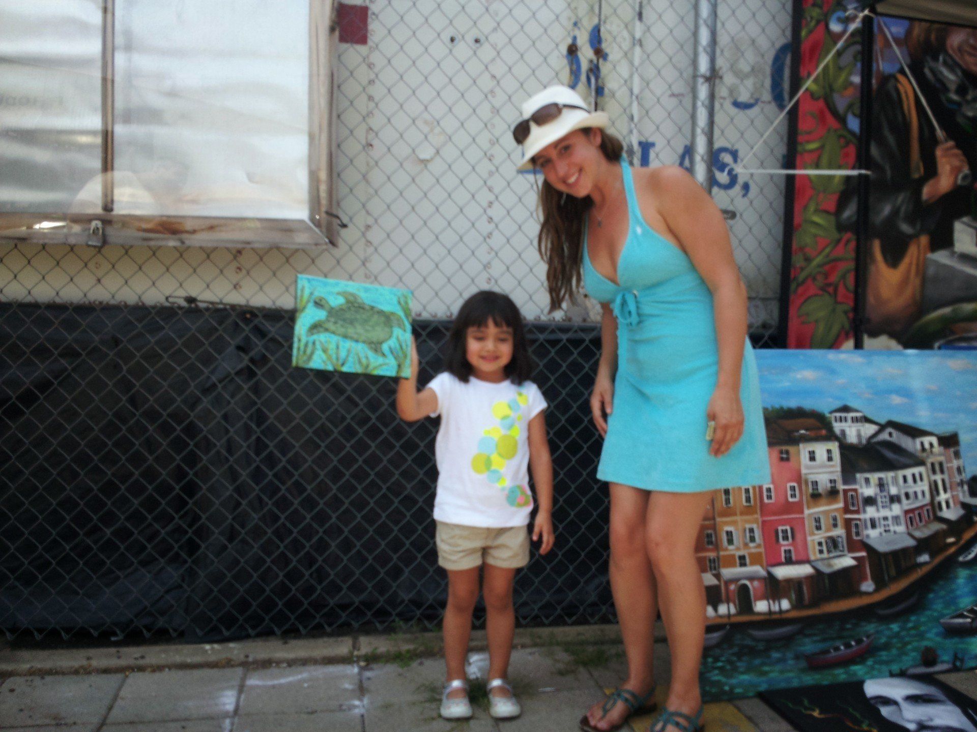 A woman in a blue dress stands next to a little girl holding a painting
