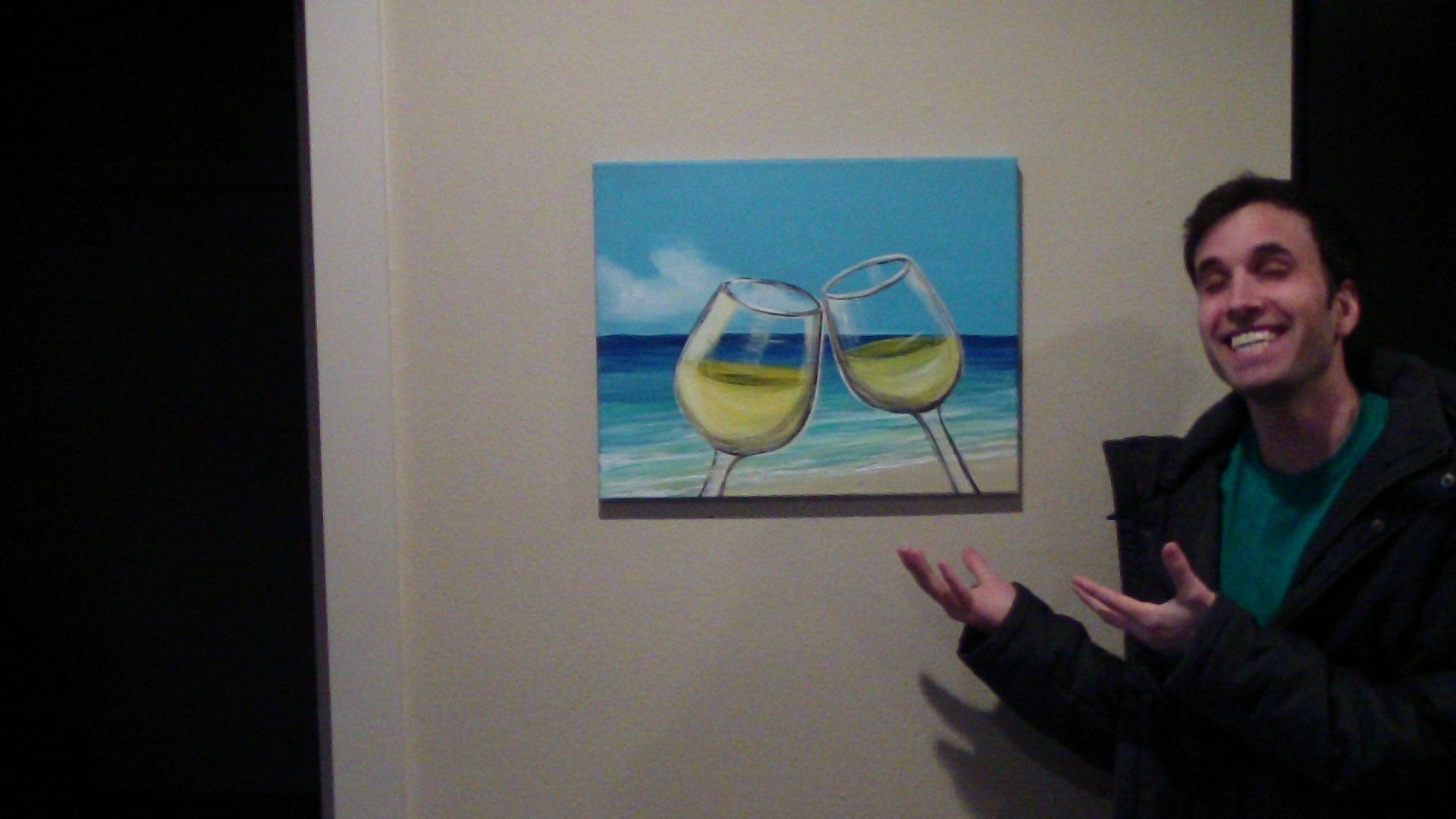 A man is standing in front of a painting of two wine glasses on a beach