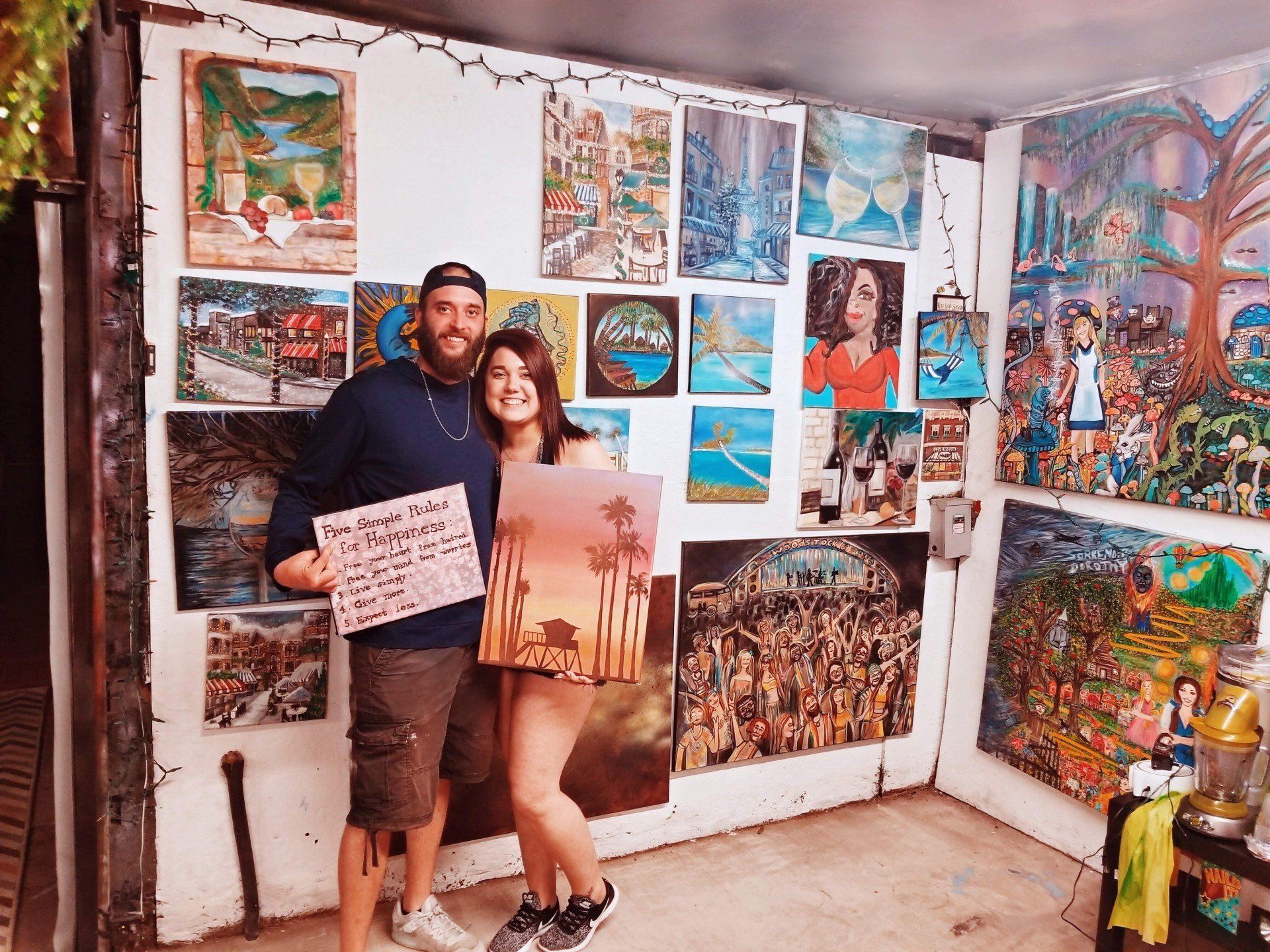 A man and a woman are standing in a room holding paintings.