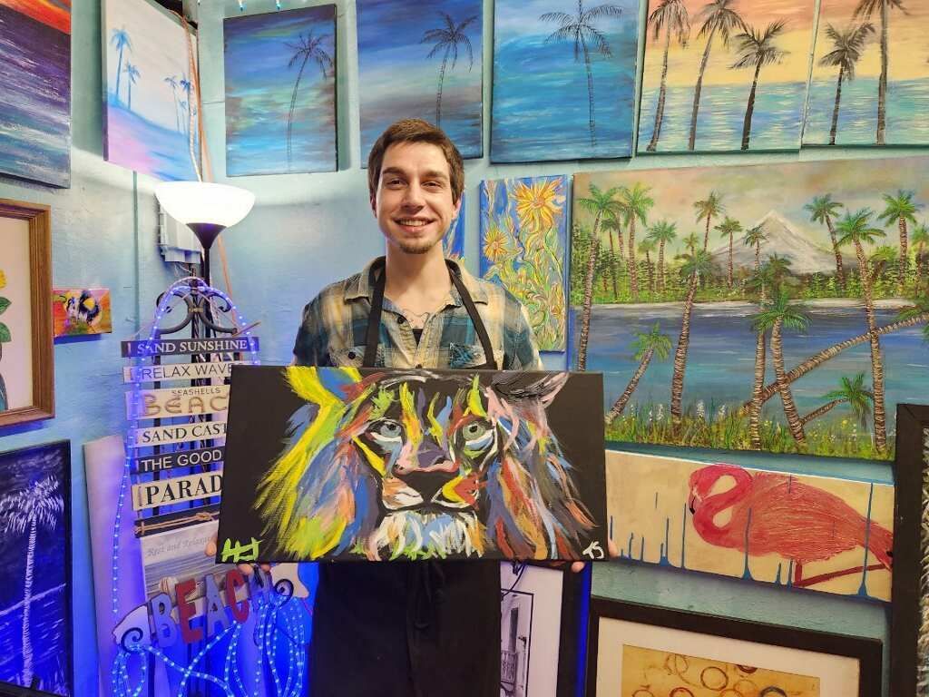 A man is holding a painting of a lion in front of a wall of paintings.