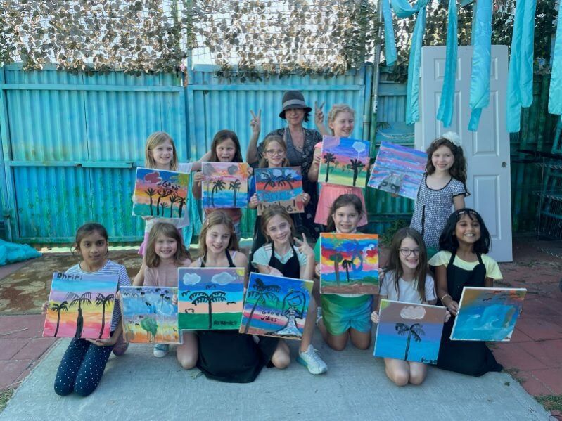 A group of young girls are posing for a picture with their paintings.