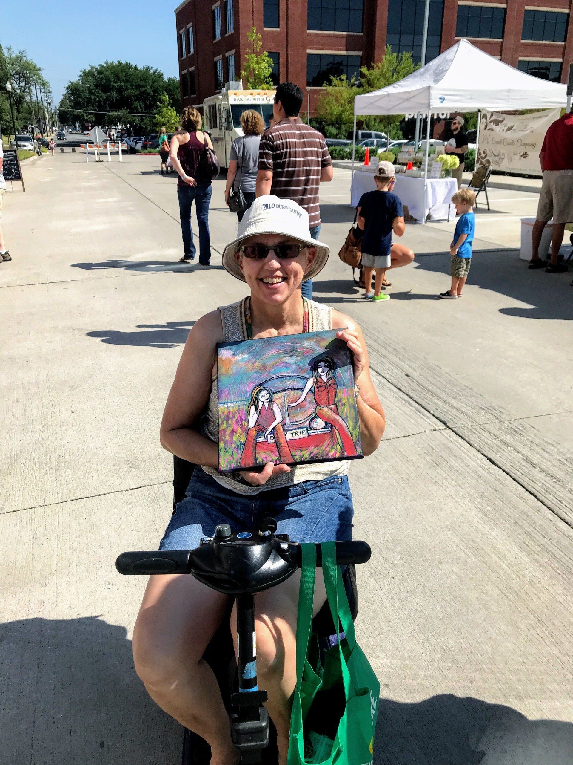 A woman is sitting on a scooter holding a painting.