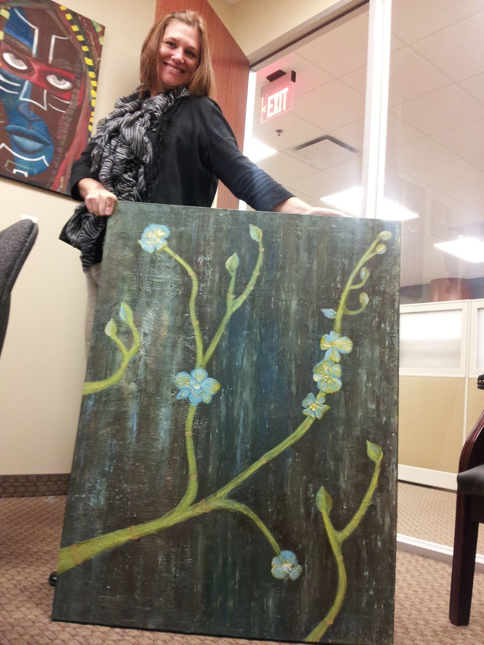 A woman is holding a large painting with flowers on it