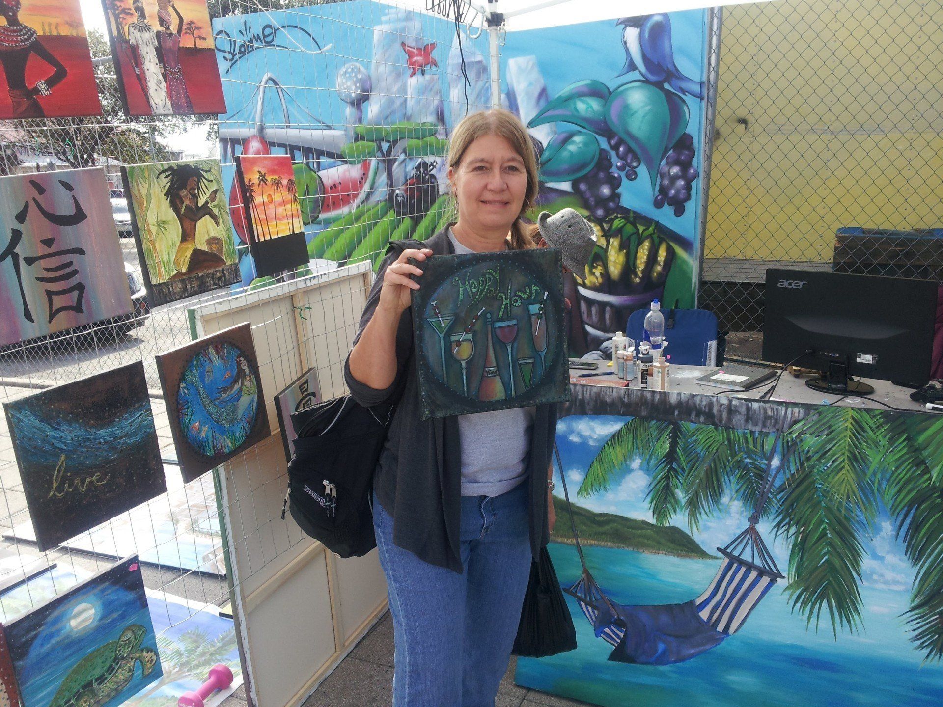 A woman is holding a painting in front of a display of paintings