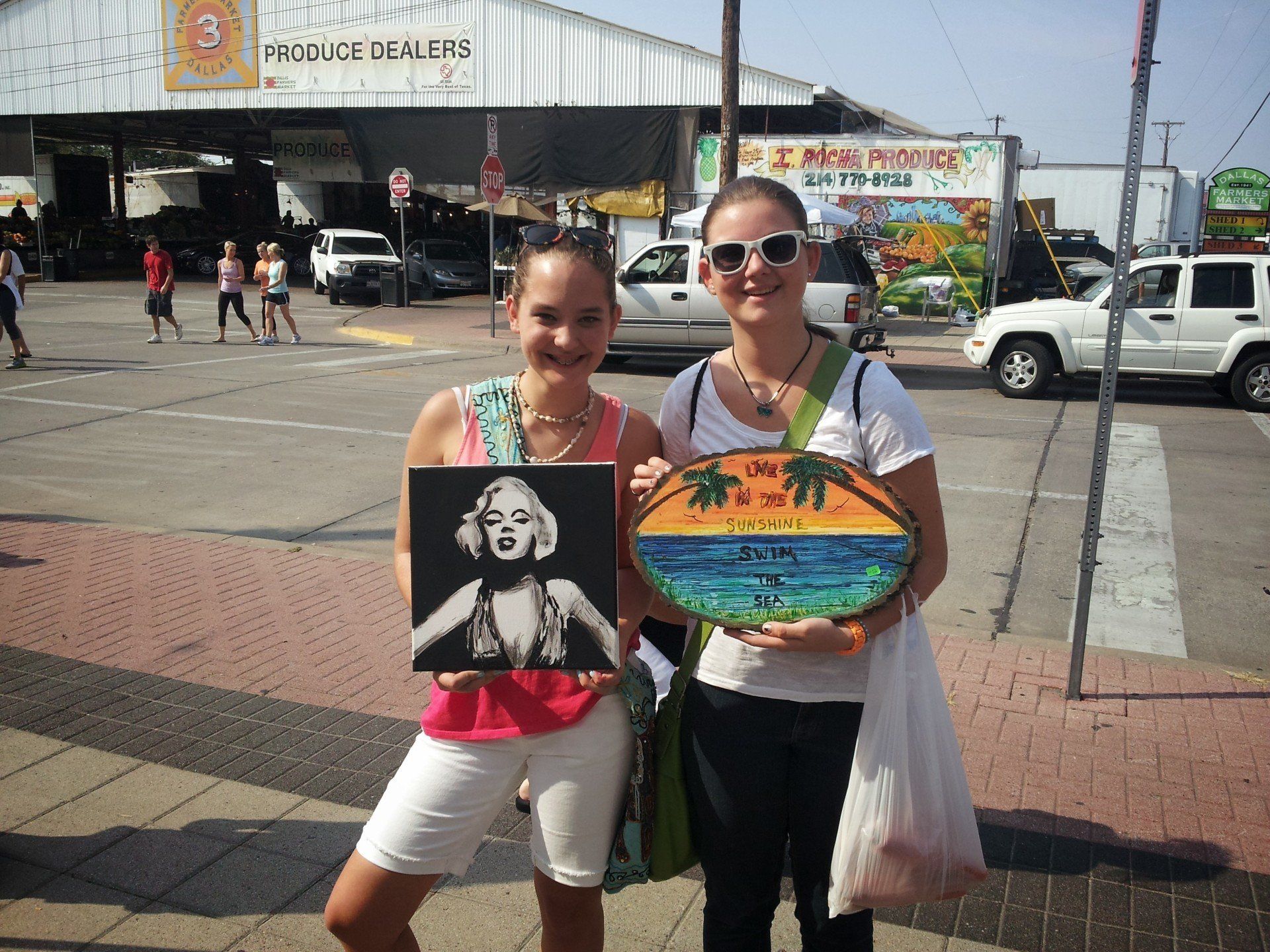 Two women are holding a painting of marilyn monroe