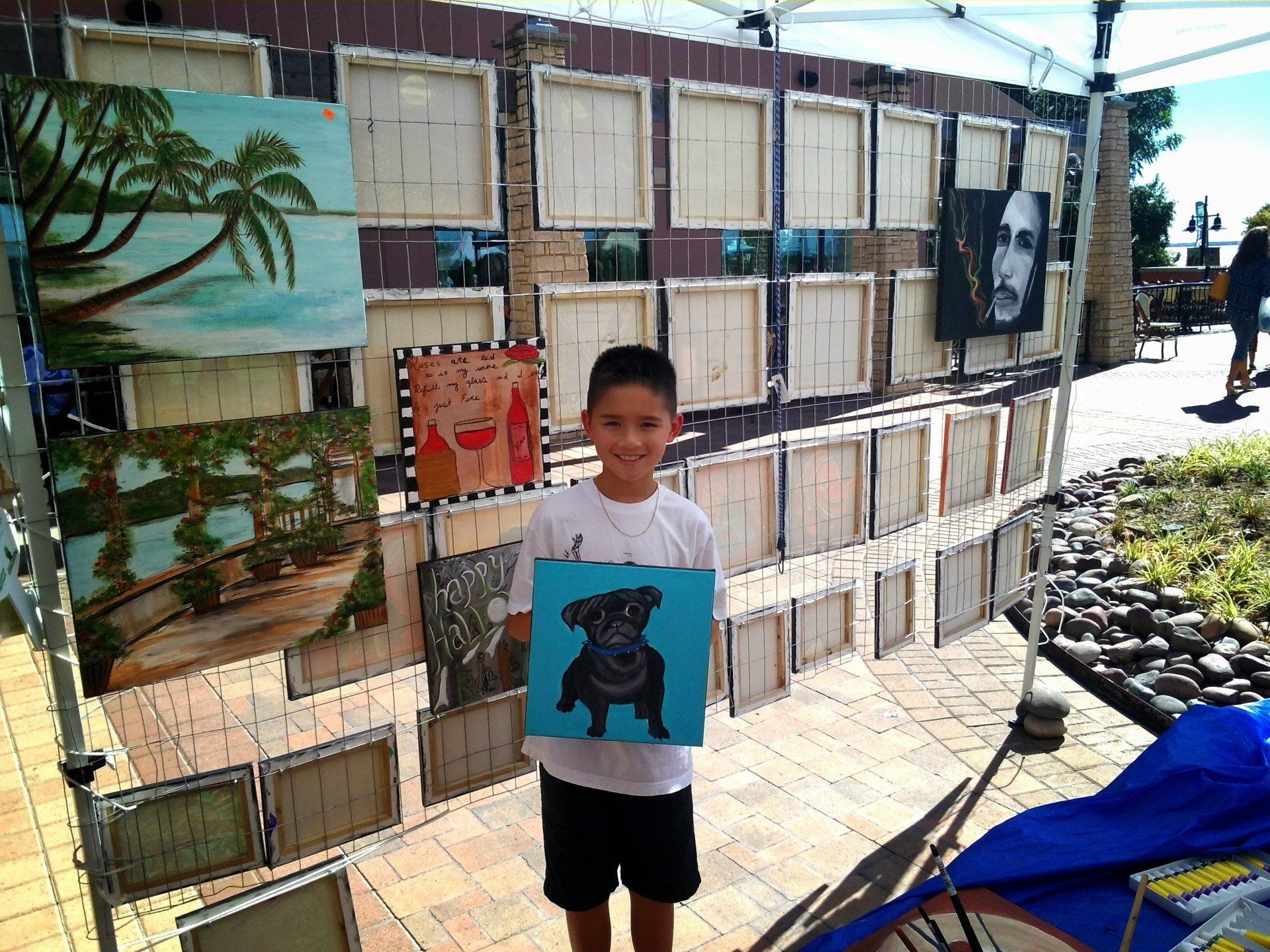 A young boy is holding a painting of a dog in front of a wall of paintings