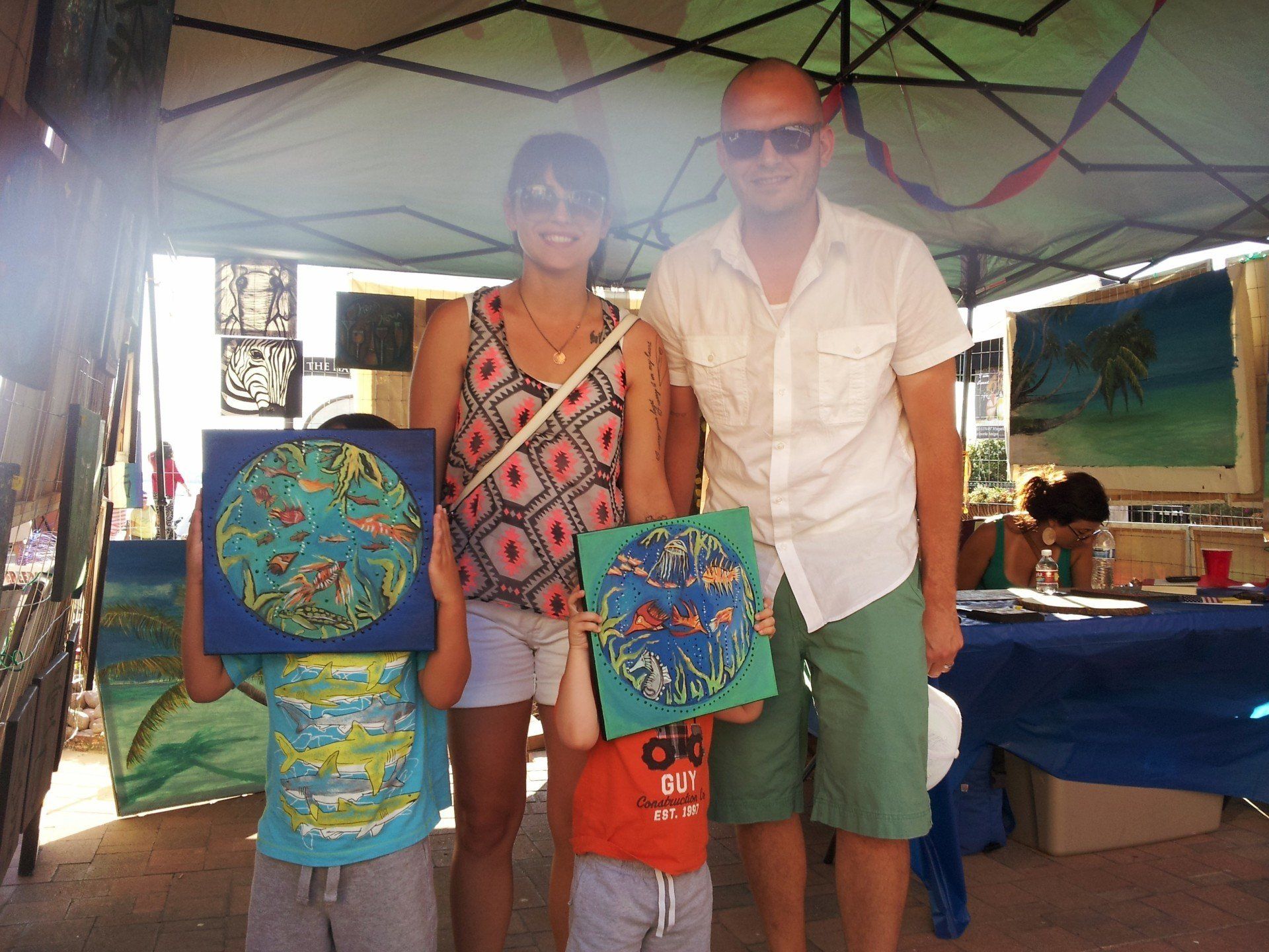 A group of people standing under a tent holding paintings