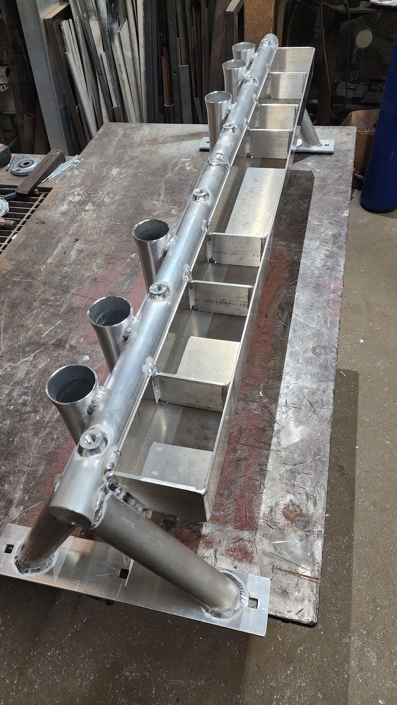 Metal fabricated structure with vertical tubes, horizontal trough, and supporting legs on a metal table.