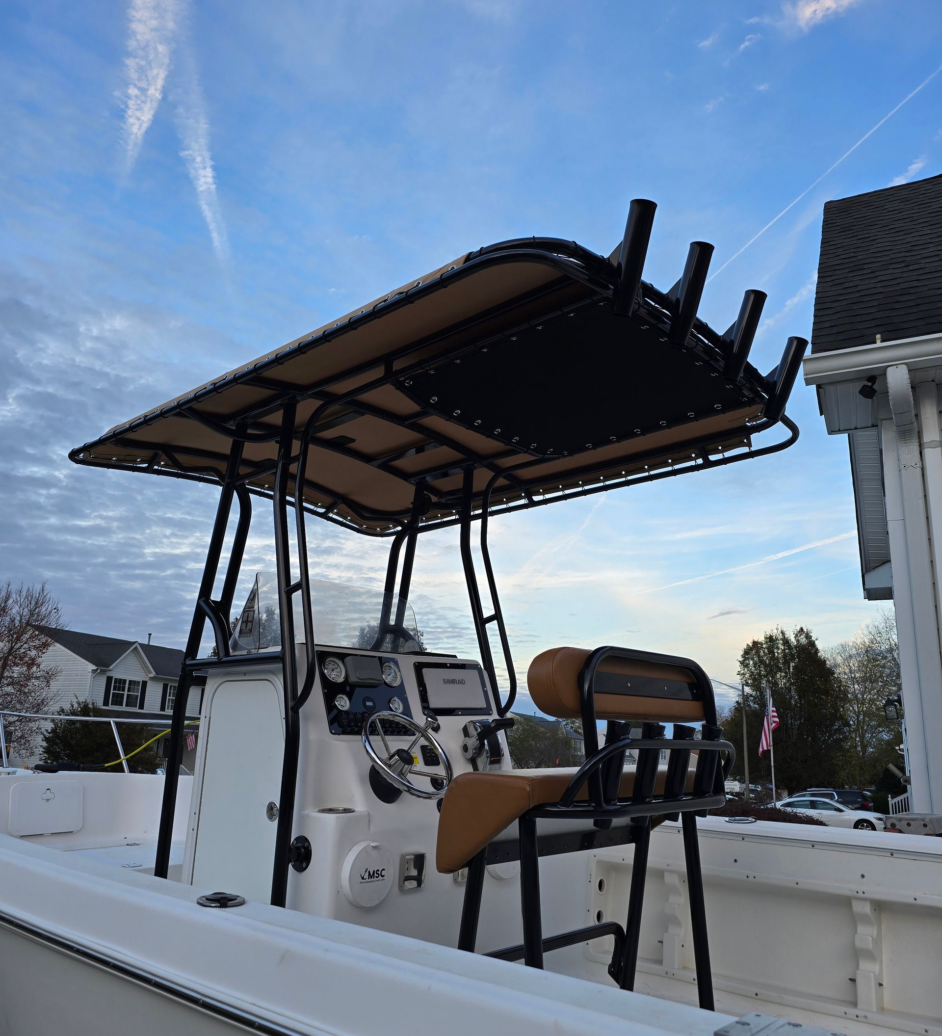 Boat with a black frame and tan canopy, with a brown seat in front of a blue sky.