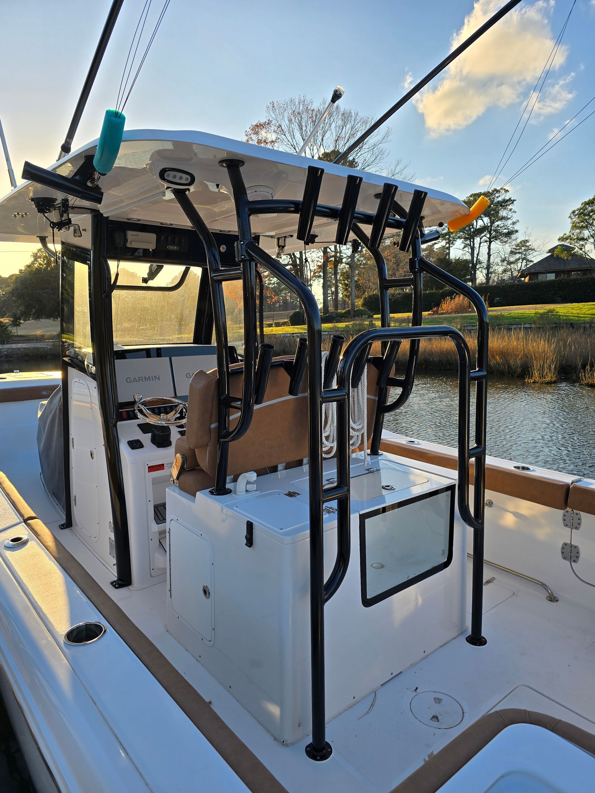 Boat with black frame, fishing rod holders, and tan seats, docked near water.