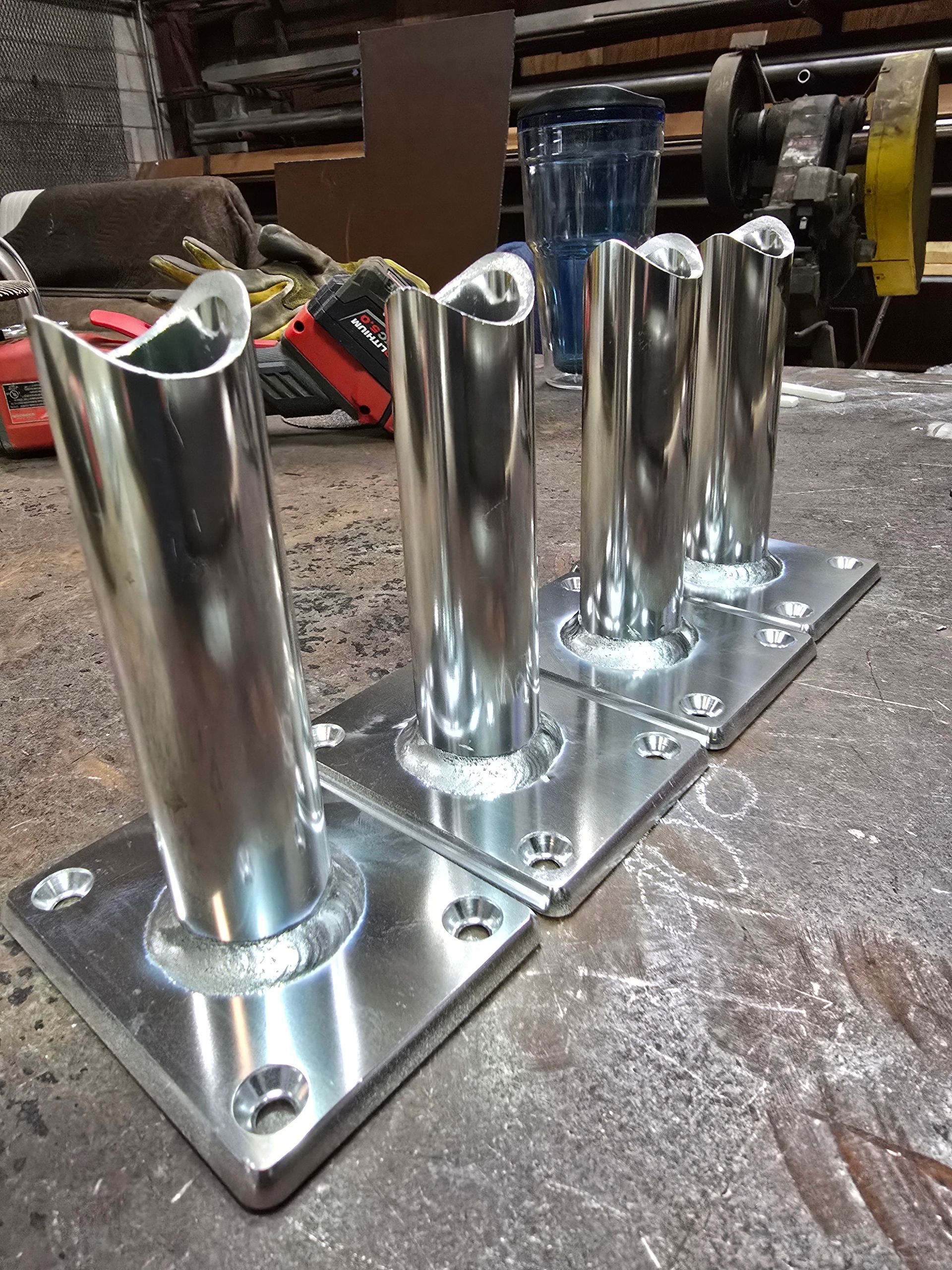 Four shiny metal pole bases welded to square plates on a workshop surface.