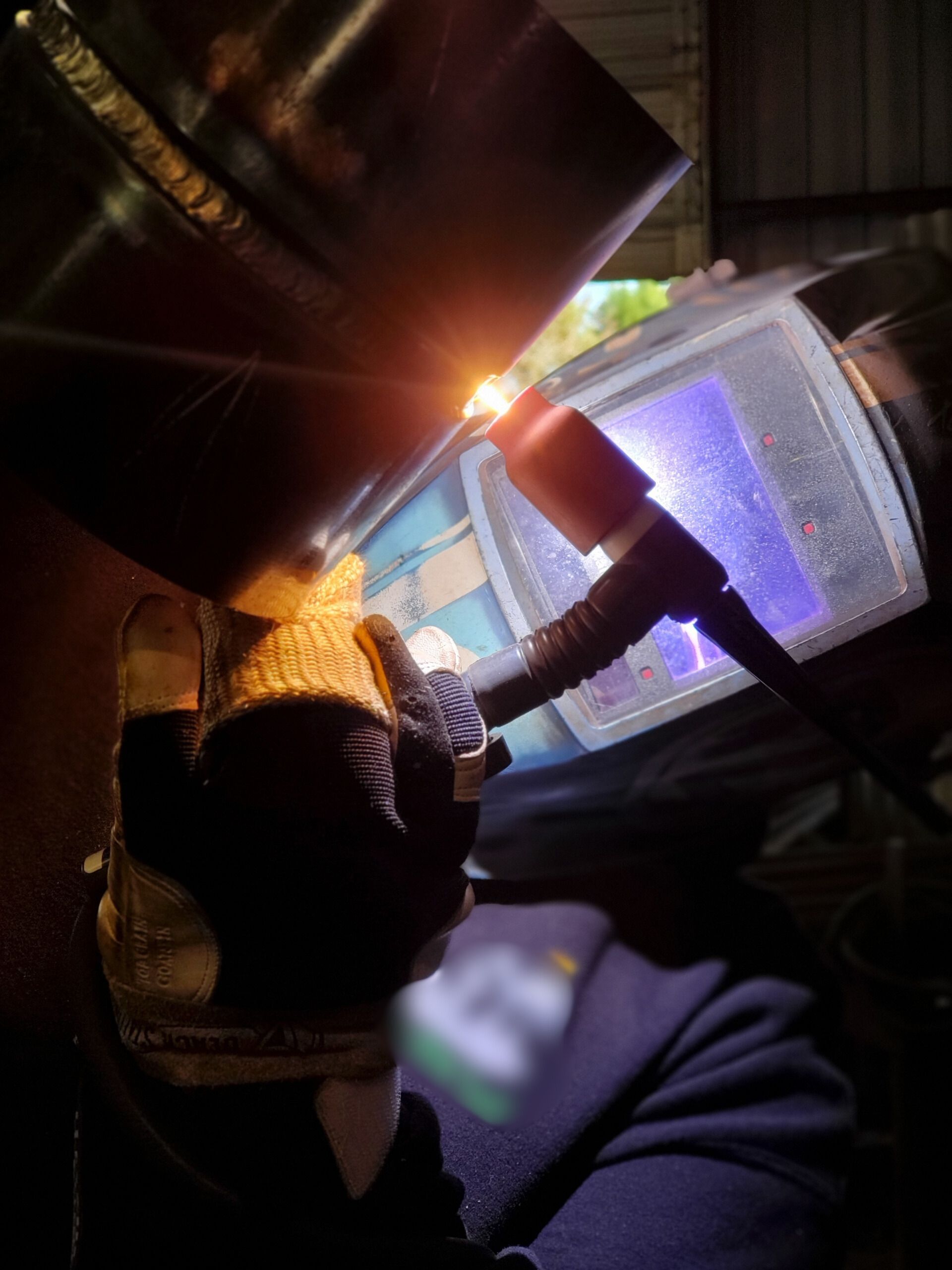 Welder wearing a helmet, welding a metal pipe. Bright sparks illuminate the work area.