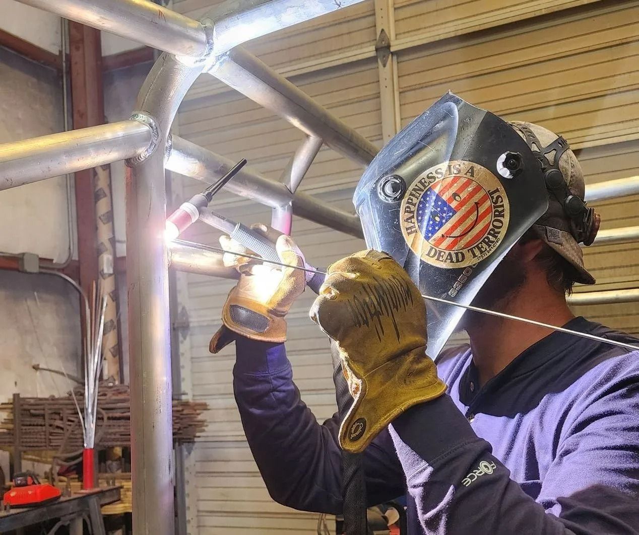 Welder with protective mask, gloves, and clothing welds metal frame.