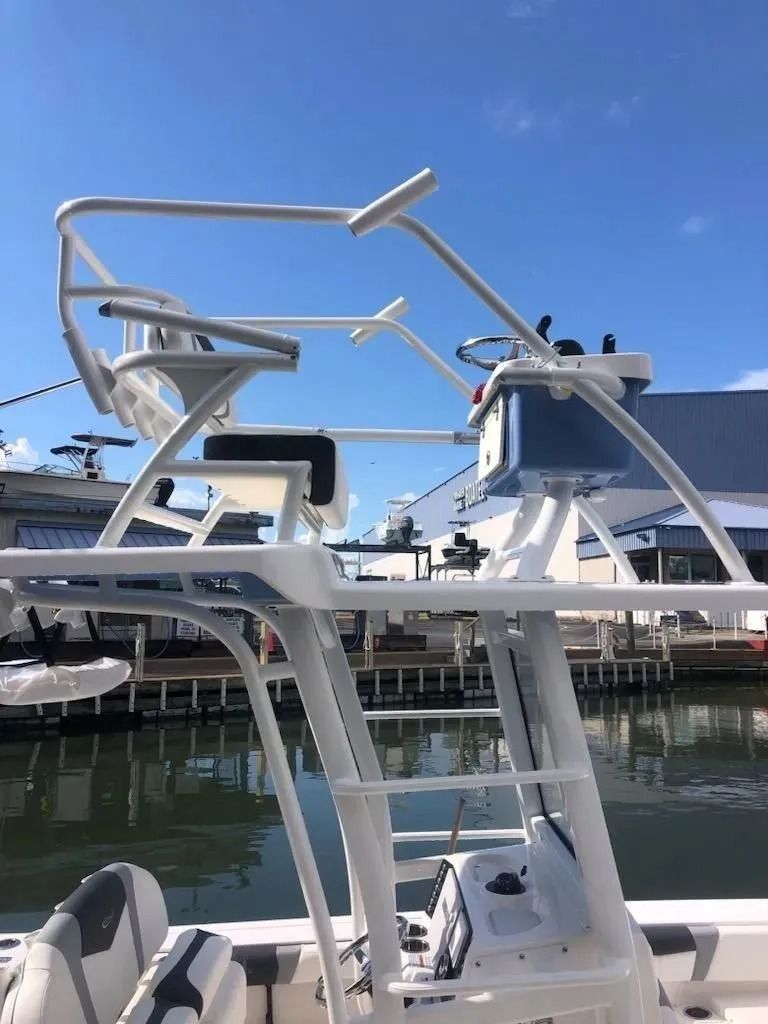 White fishing boat tower with radar, steering wheel, and seating. Waterside setting, blue sky.